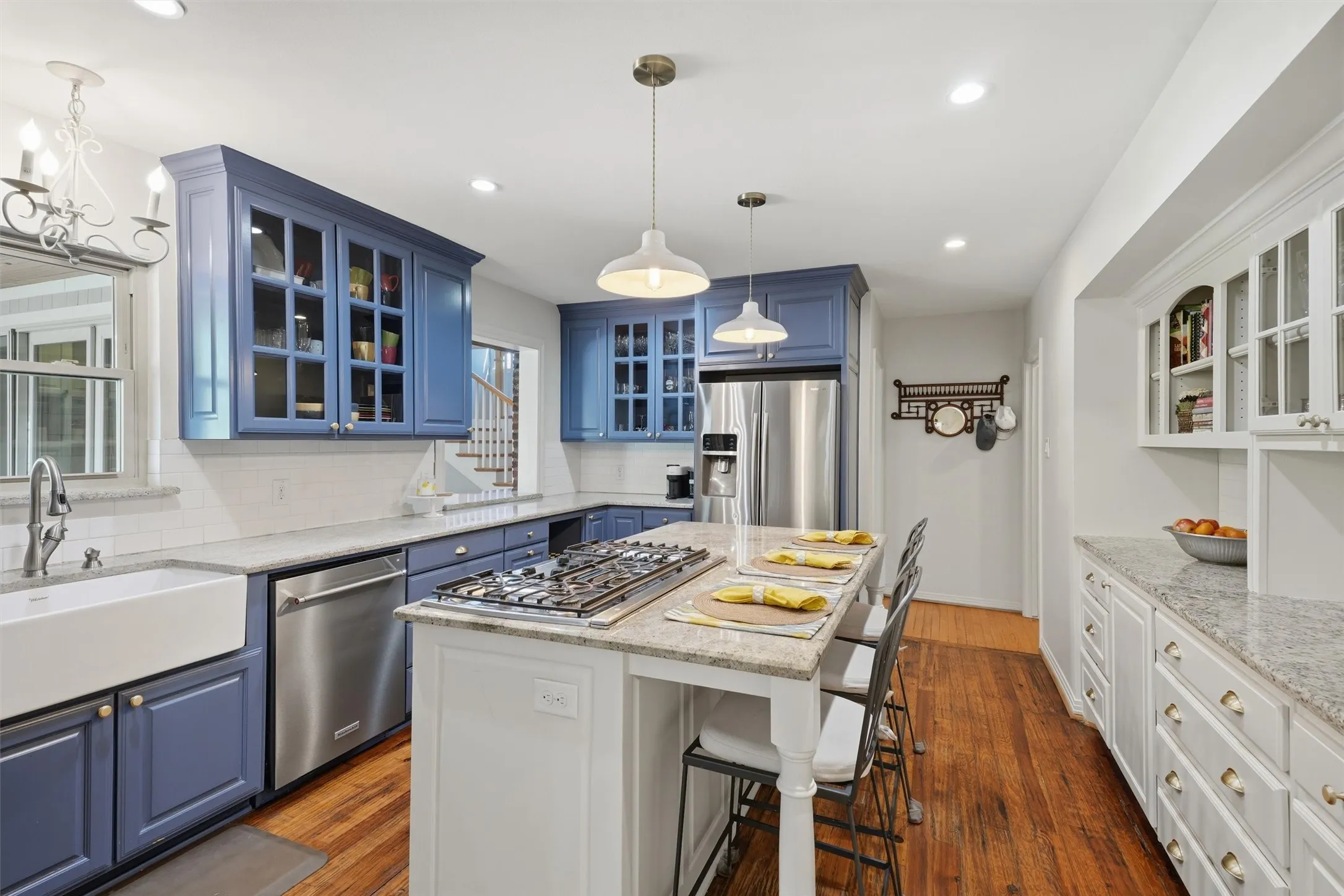 Alternate kitchen perspective highlighting the island with built-in gas cooktop and breakfast bar seating. Features an apron-front sink, stainless steel appliances, and extensive cabinetry