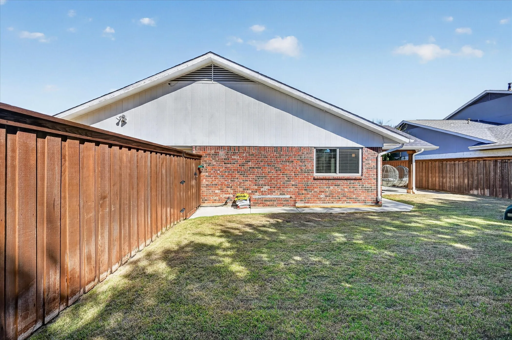 Enjoy a fenced backyard with grassy space, a brick planter box and a walkway leading to the covered patio.