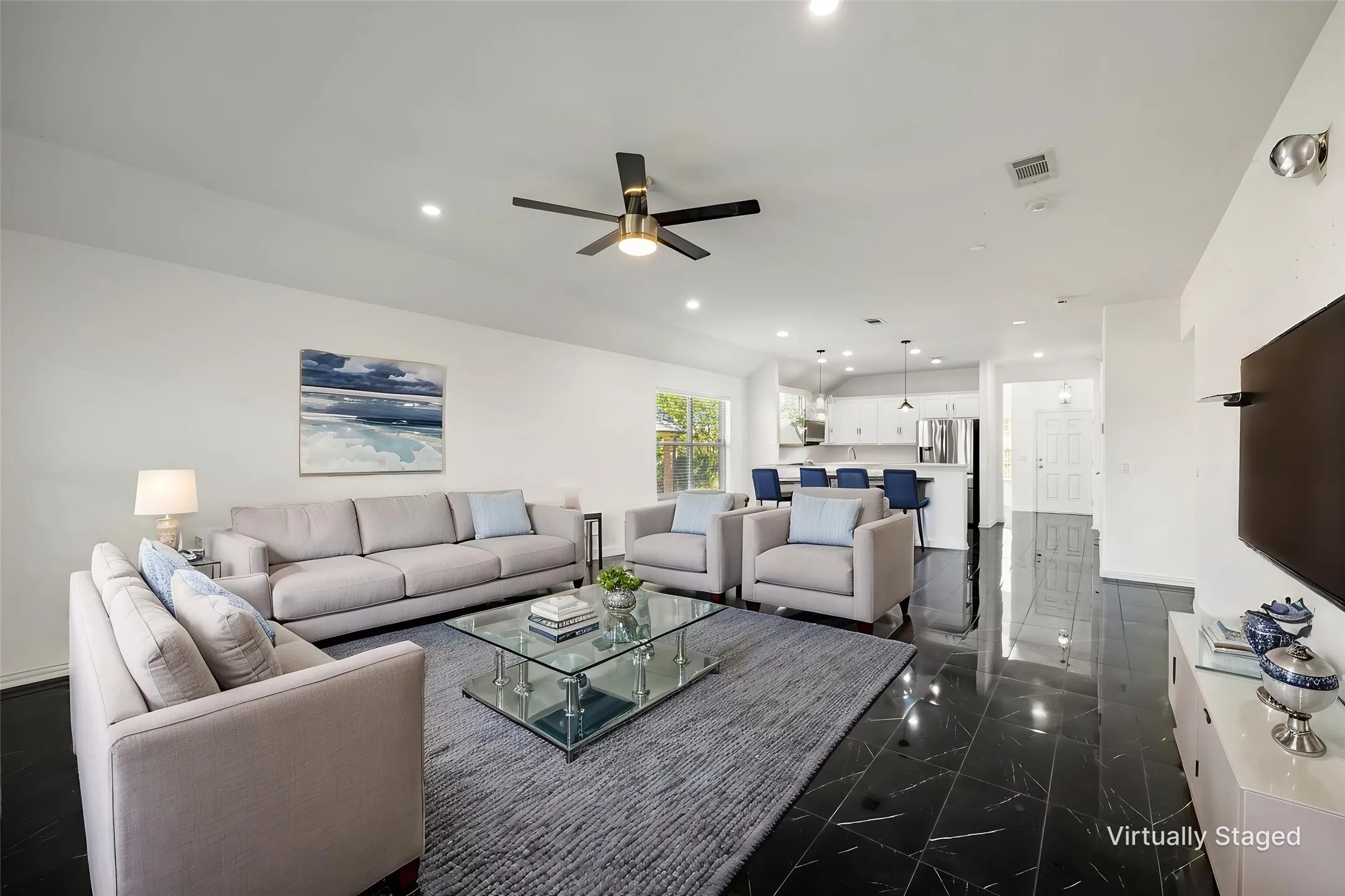 Open-concept living space featuring black tile flooring, white walls, and a ceiling fan with integrated lighting