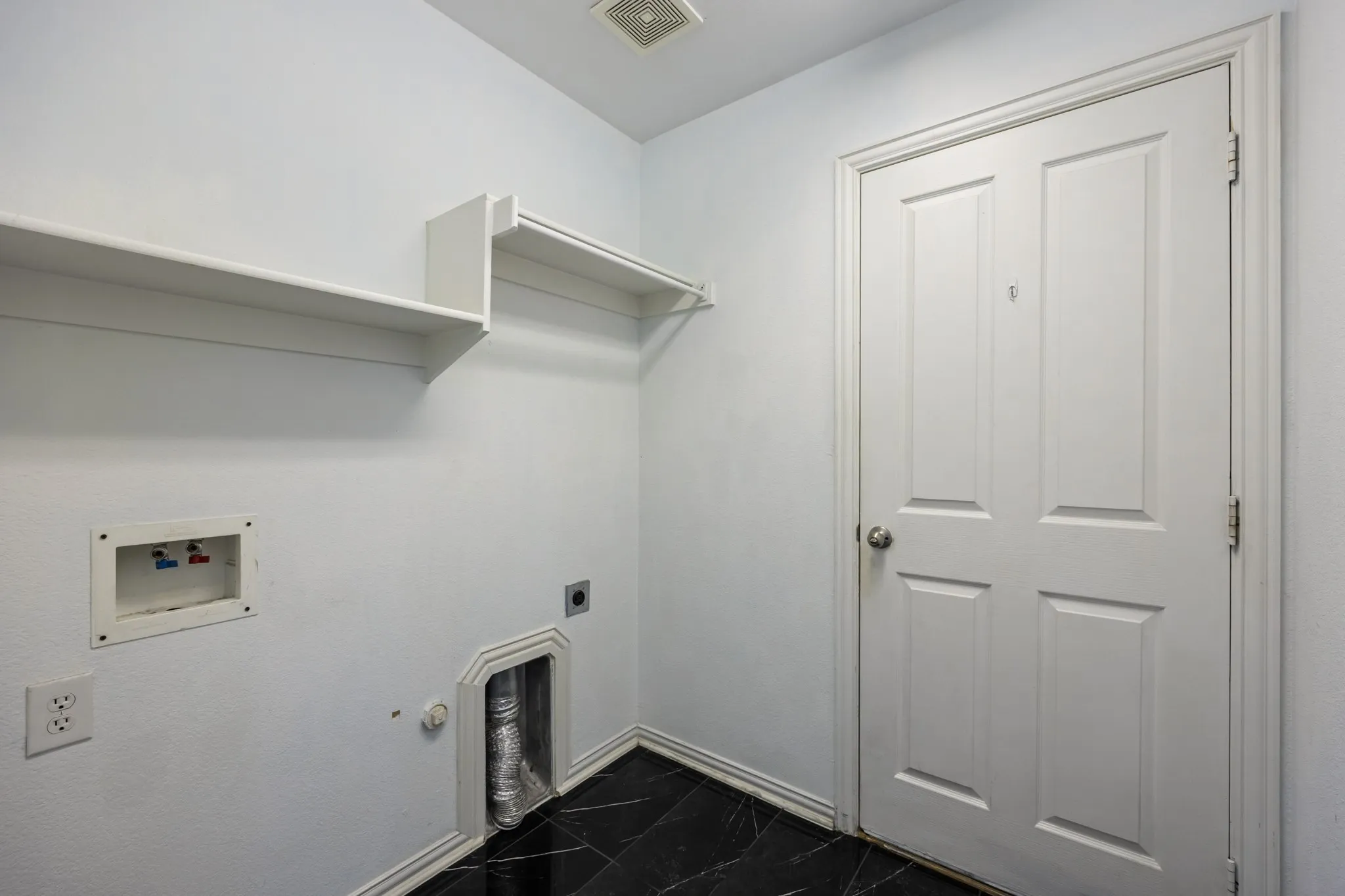 Laundry area featuring built-in shelving, a panel door, black tile flooring, and utility hookups