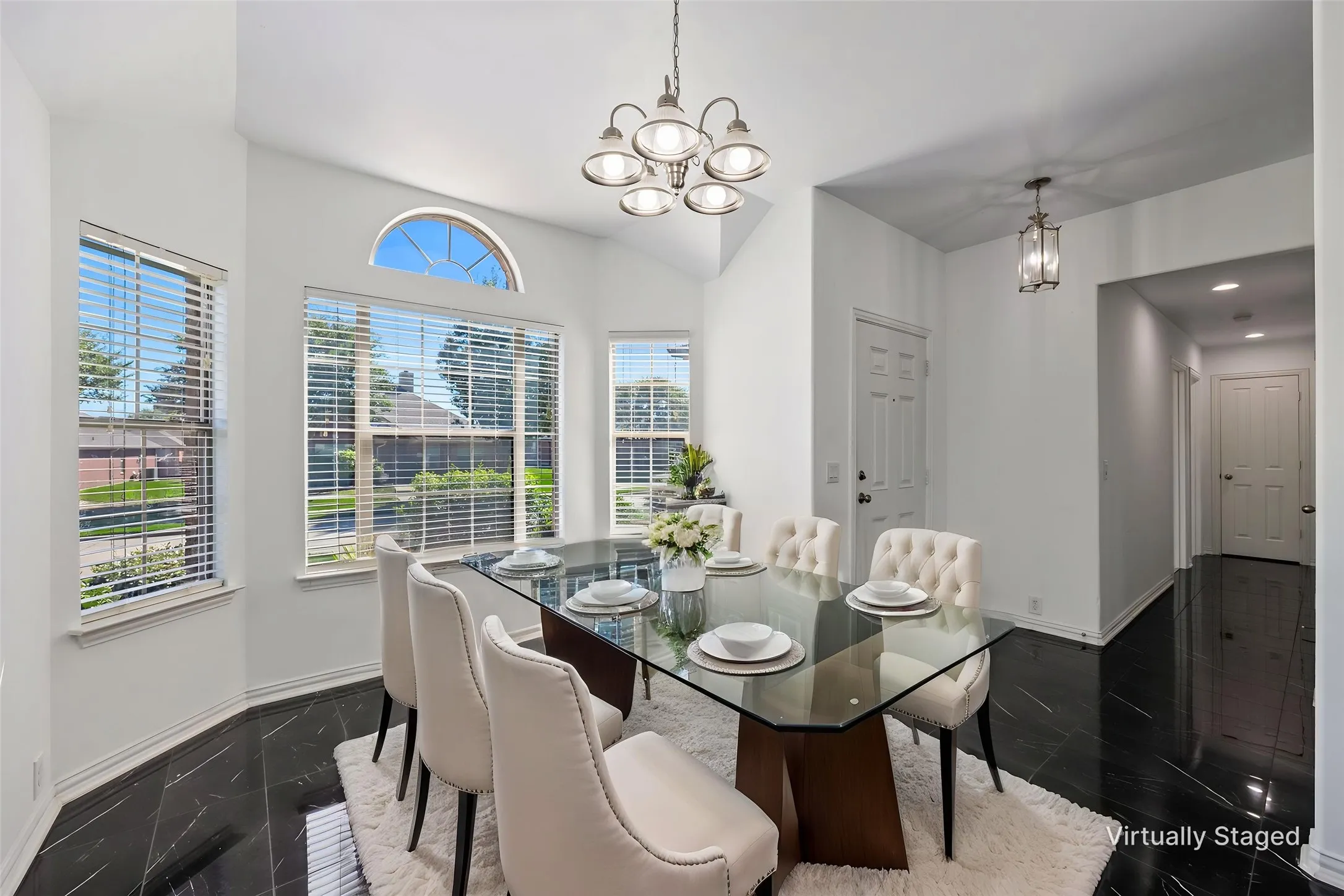 Vaulted ceiling with a multi-light chandelier, arched transom window, multiple windows with blinds, and black tile flooring