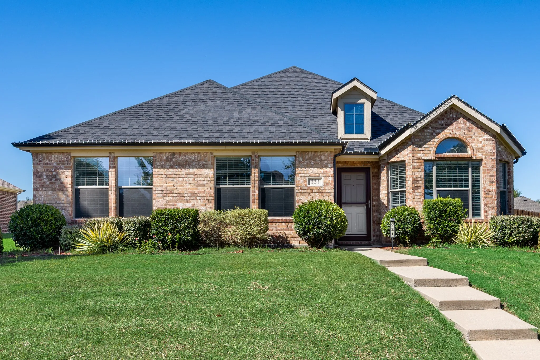 Brick exterior with a dark shingle roof, featuring a dormer window and arched transom window