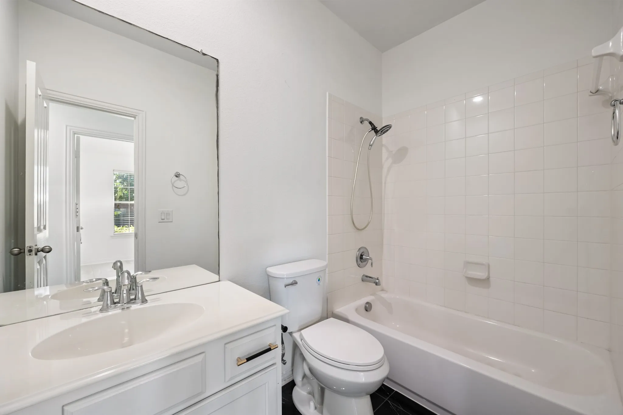 White vanity with integrated sink, chrome faucet, wall-mounted mirror, white toilet, and a white tiled shower/tub combination