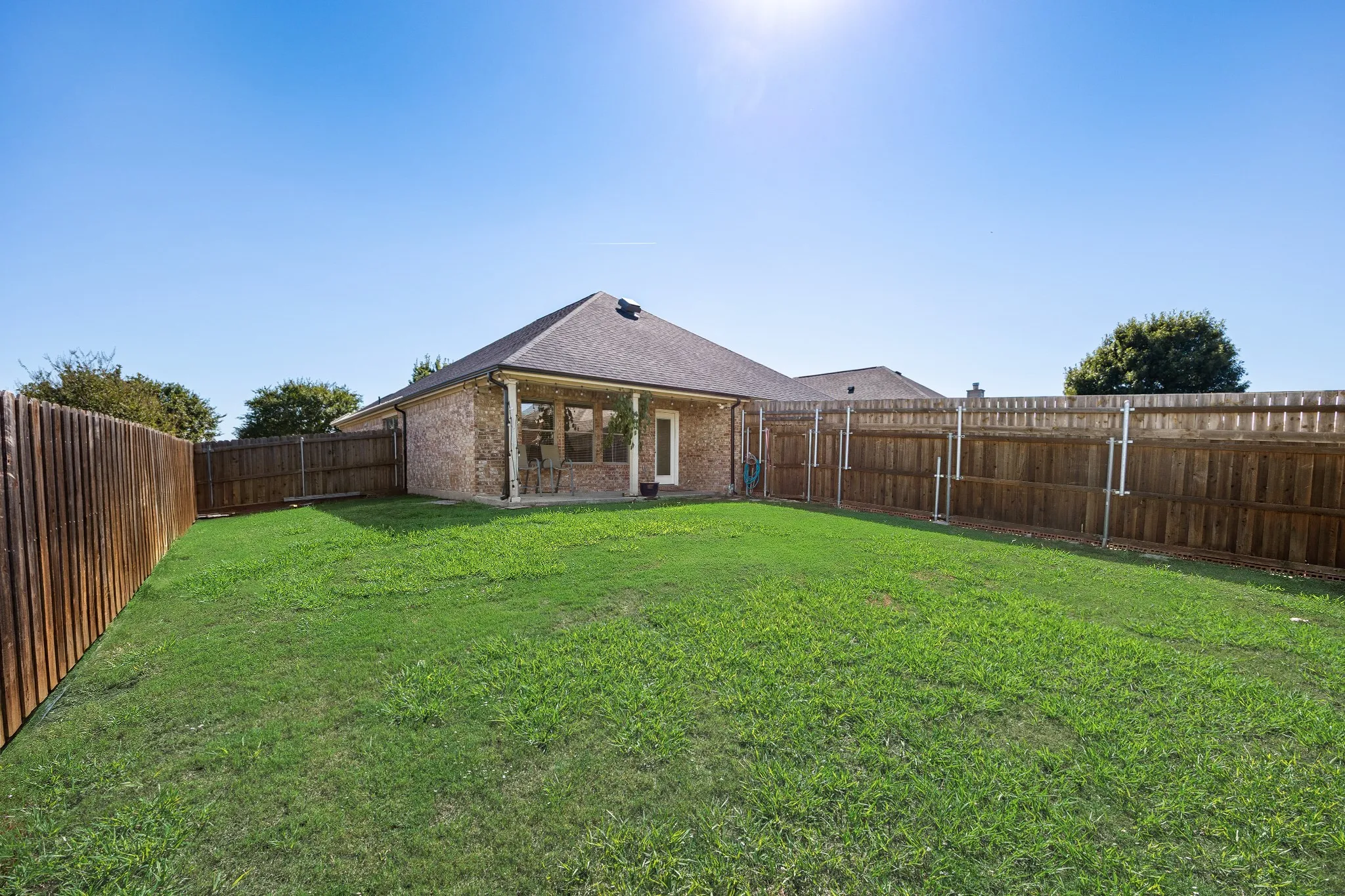 Expansive backyard with a manicured lawn, full privacy fencing, and a covered patio area