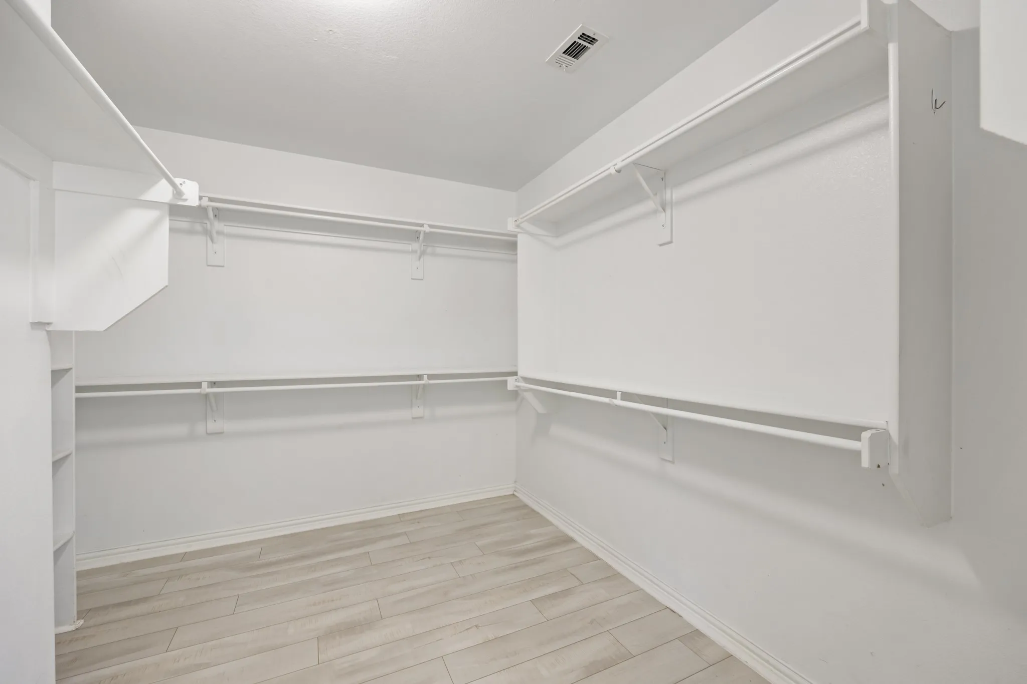 Spacious walk-in closet featuring white wood-finish flooring, built-in shelving, and multiple hanging rods