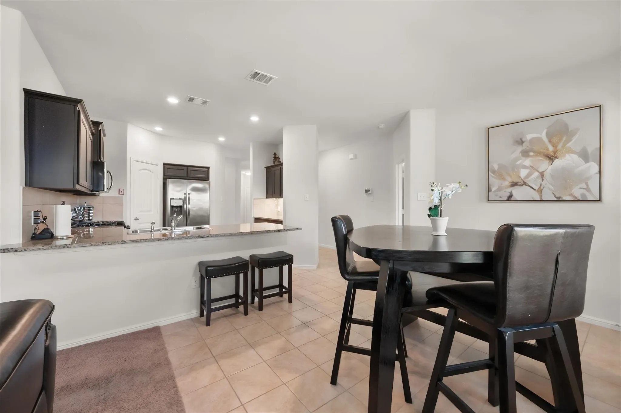 Kitchen featuring dark wood cabinetry, stainless steel appliances, a breakfast bar with granite-style countertop, and tile flooring