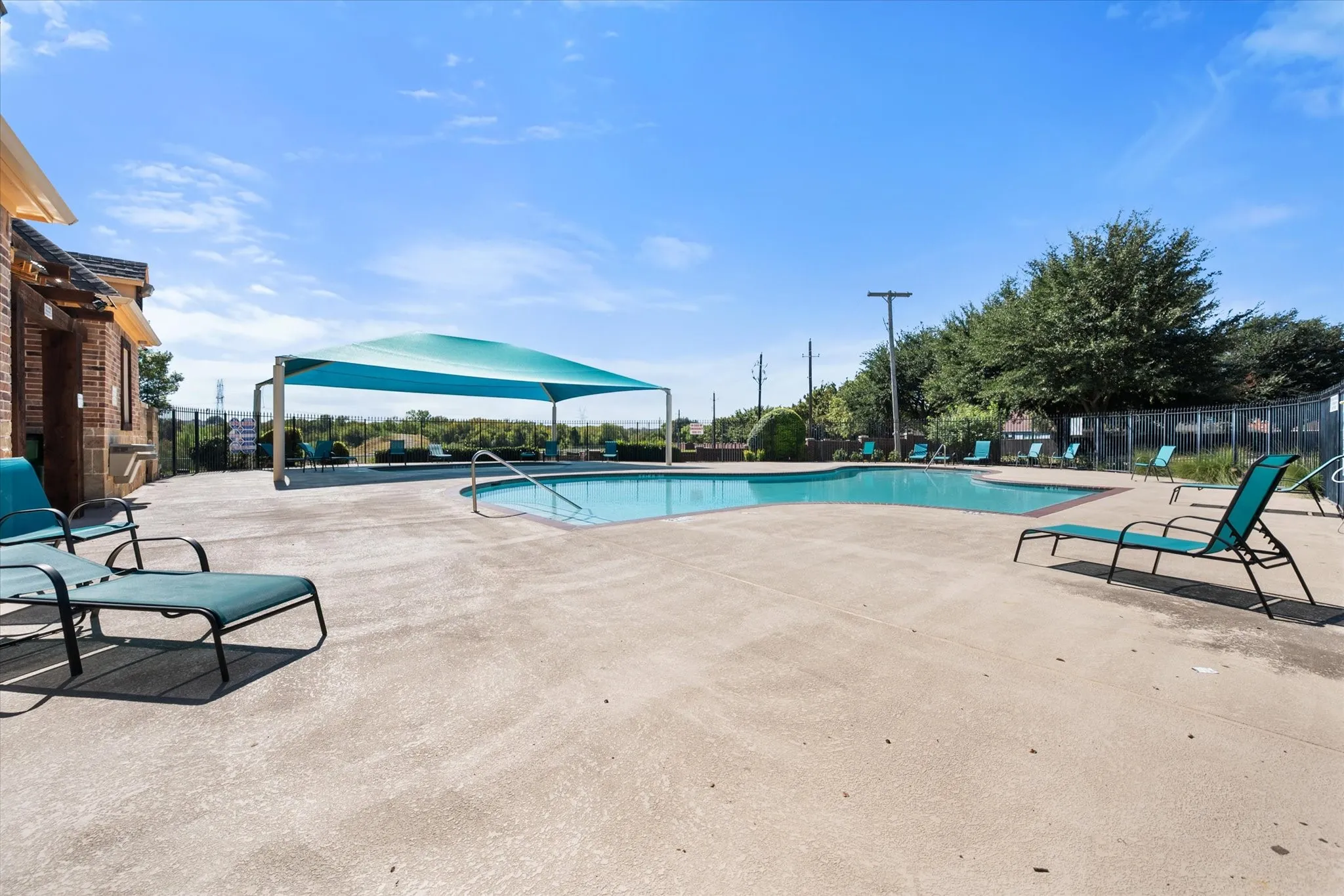 Swimming pool with concrete decking, a partial shade structure, and perimeter fencing