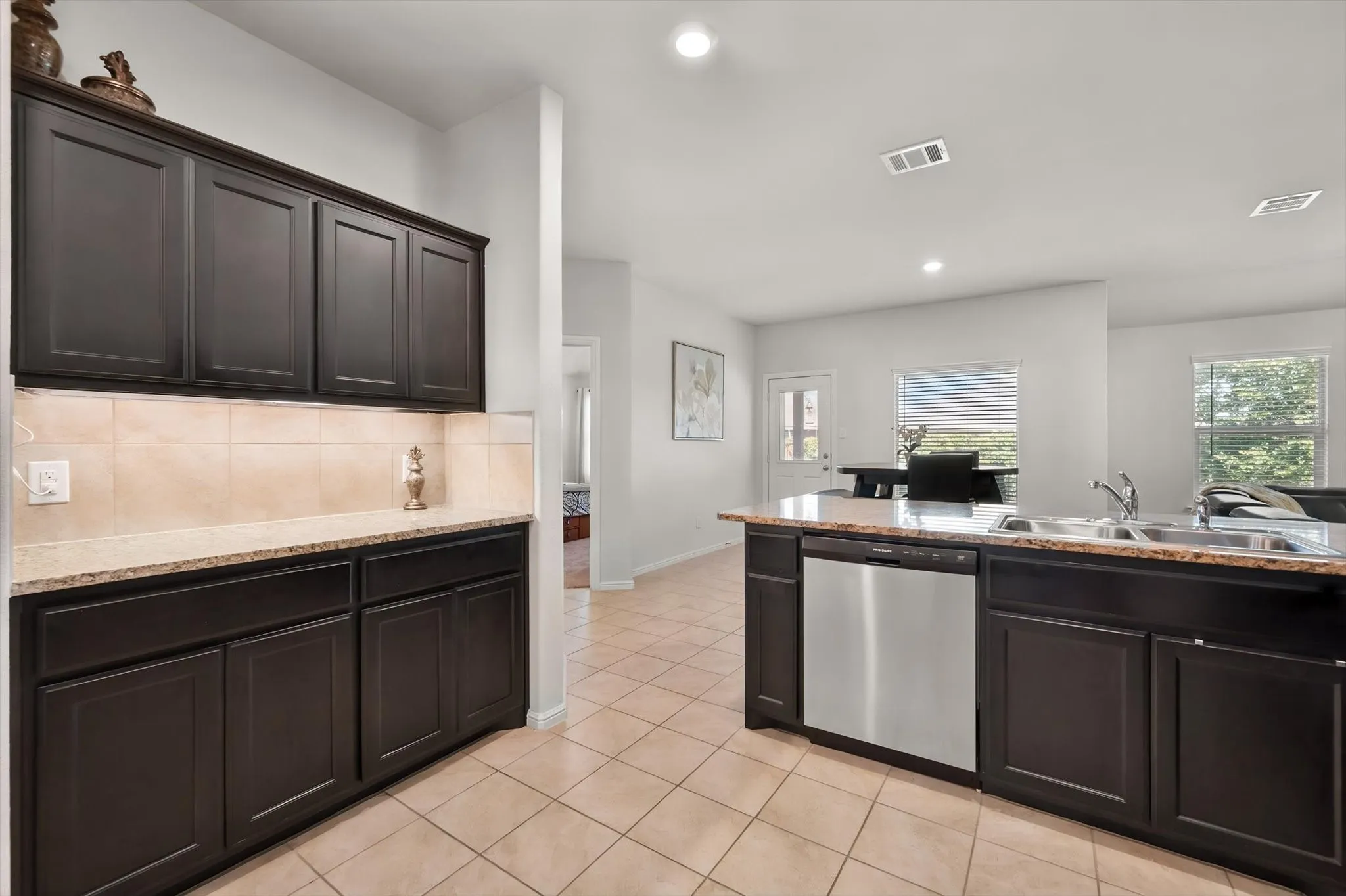 Kitchen featuring dark wood cabinetry, granite-style countertops, stainless steel dishwasher, and tiled flooring