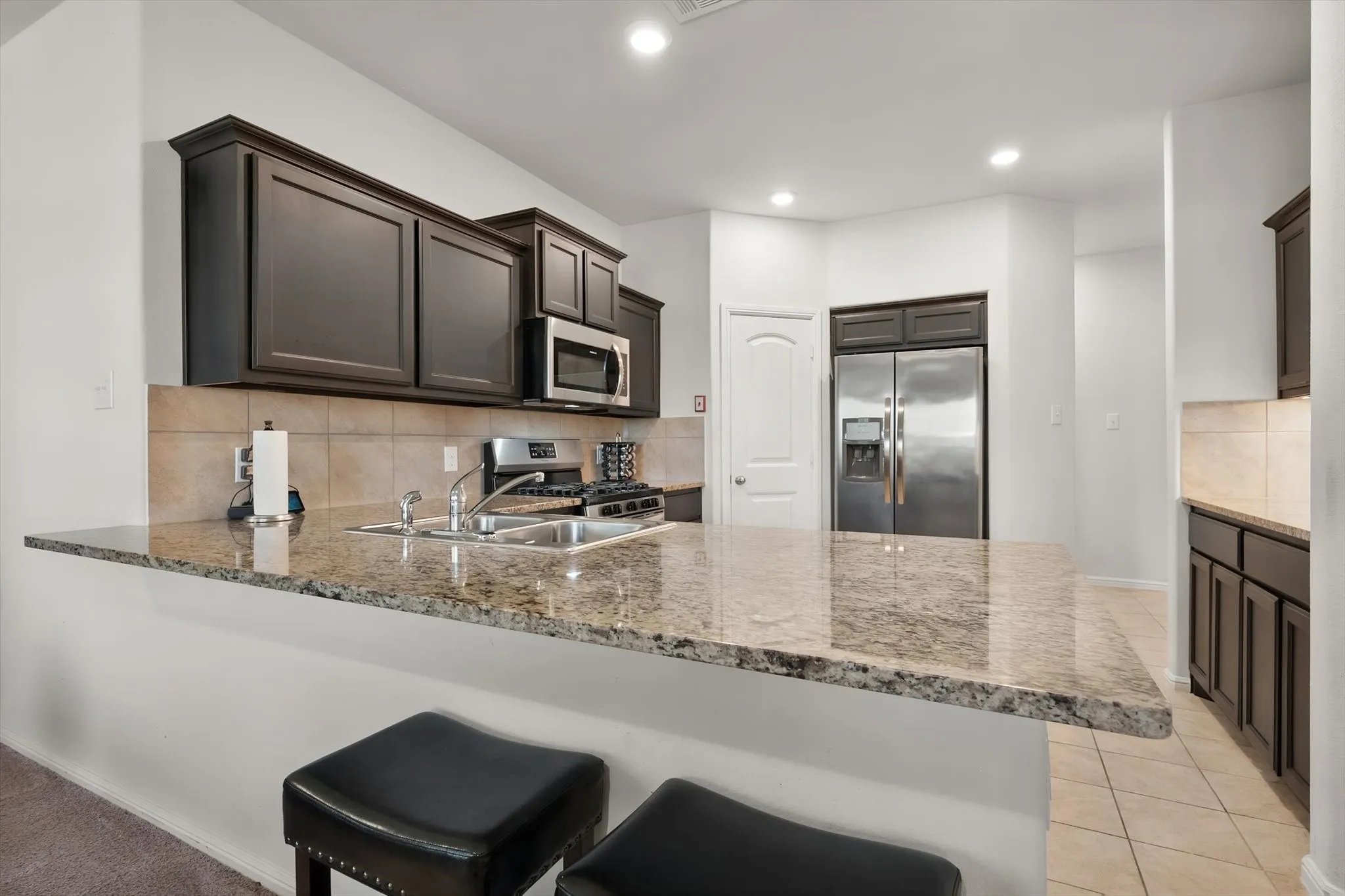 Kitchen featuring dark wood-finish cabinetry, a large breakfast bar with a stone-finish countertop, stainless steel appliances, and tile flooring