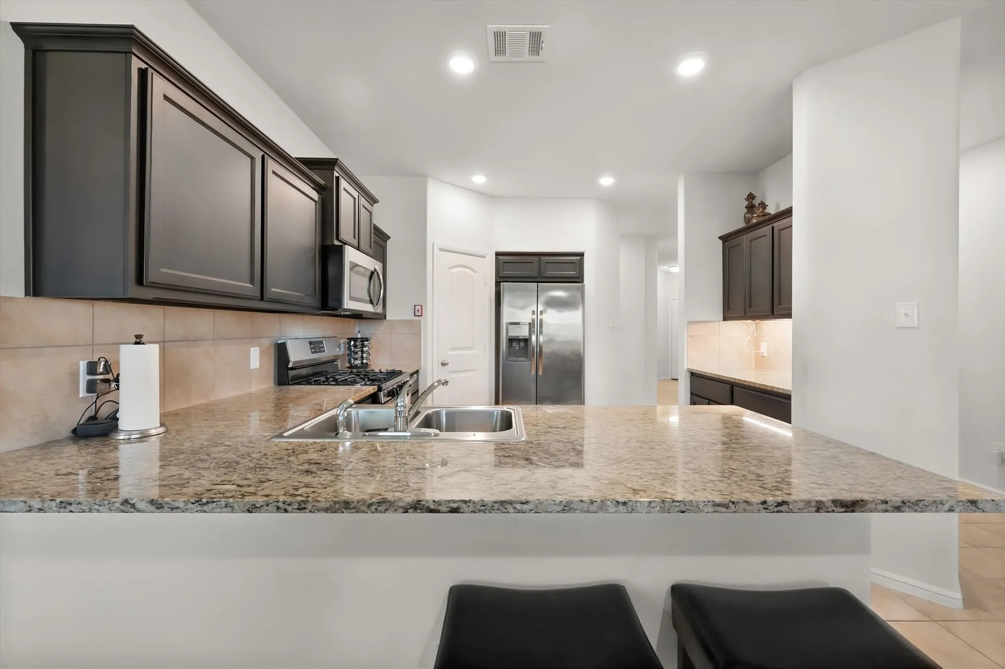Granite countertops, dark wood-finish cabinetry, stainless steel appliances, tile backsplash, and recessed lighting