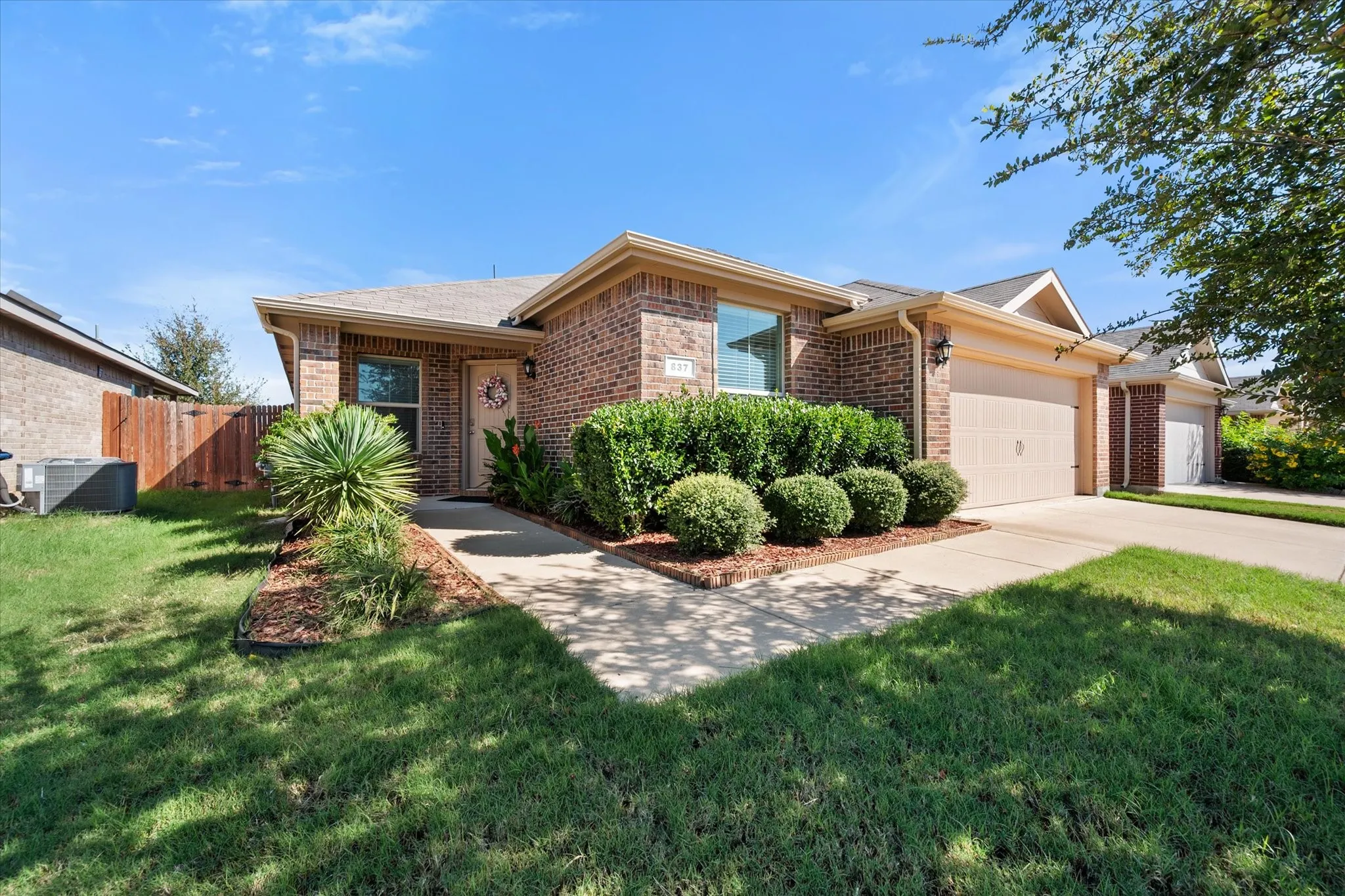 Brick exterior with an attached garage, paved driveway, and established landscape beds