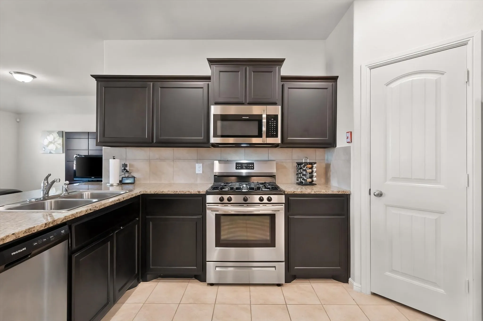 Kitchen featuring dark wood cabinetry, light-colored countertops, stainless steel appliances, and tile flooring
