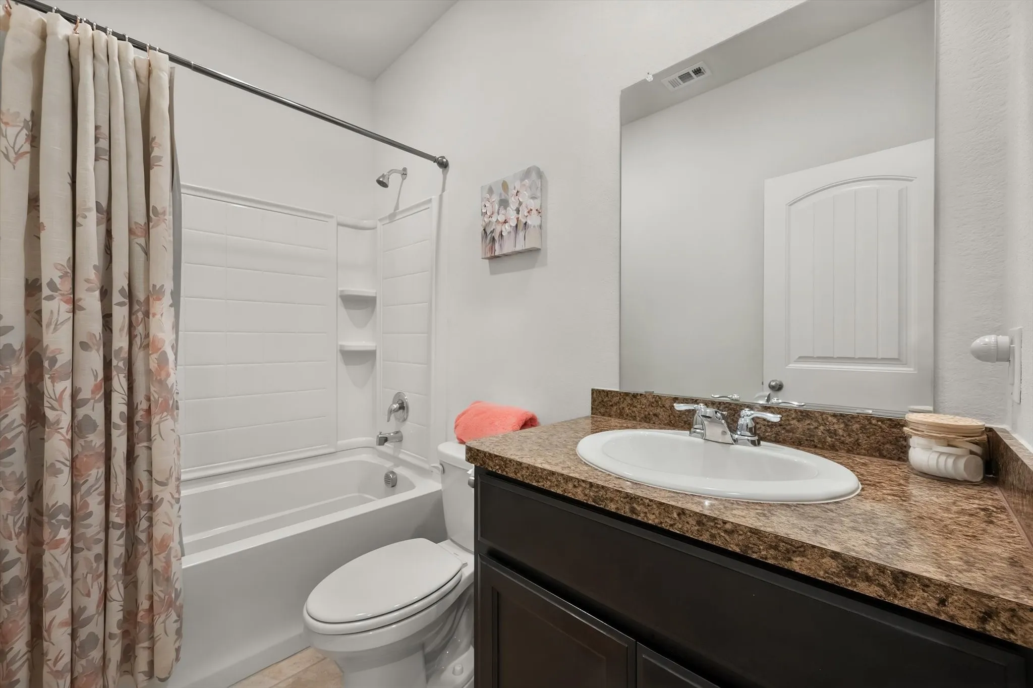 Bathroom featuring a full-sized tub with shower, dark wood-finish vanity, and a speckled countertop with an integrated sink