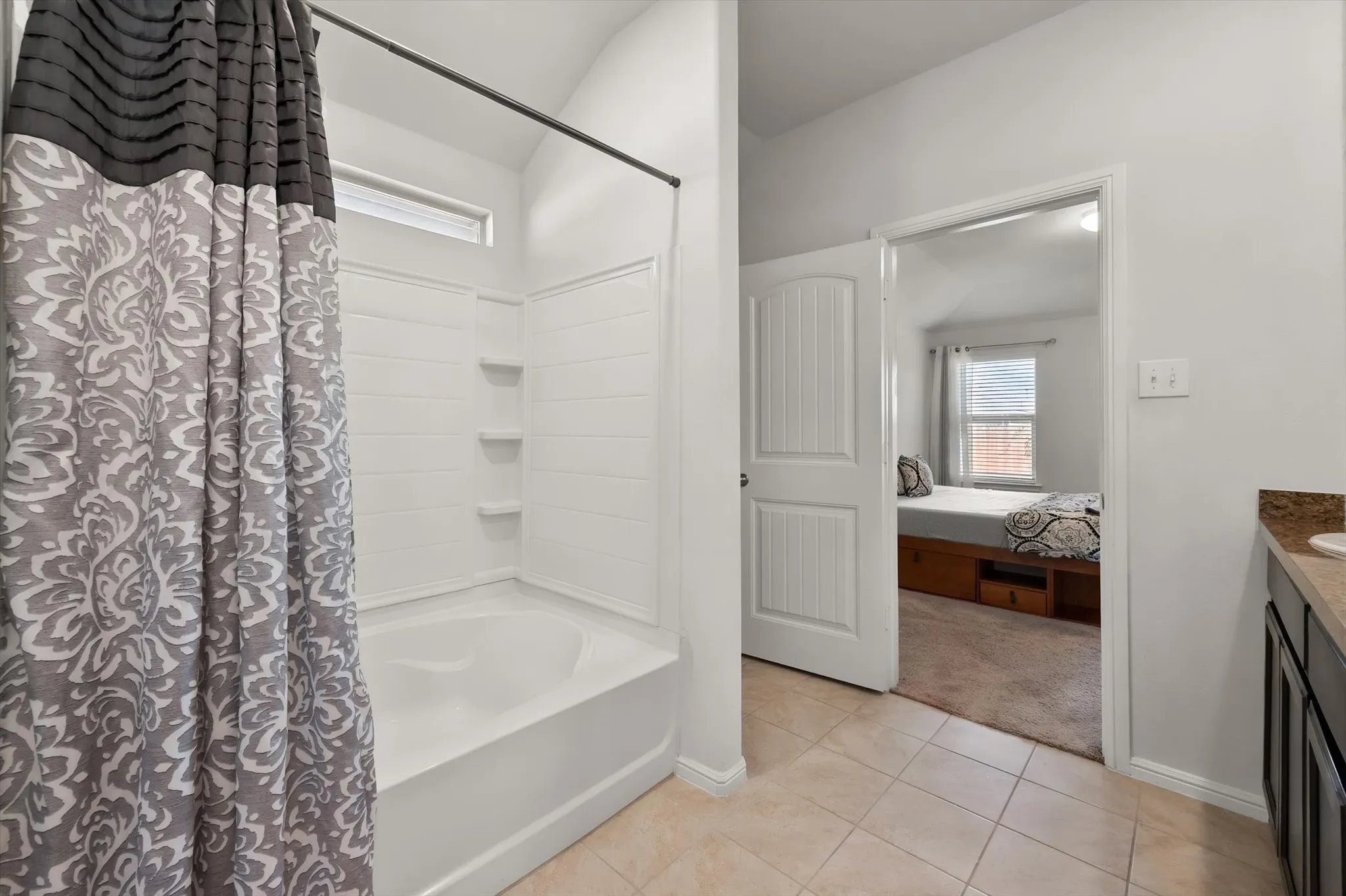 Bathtub with white surround and integrated shelving, transom window, and tile flooring