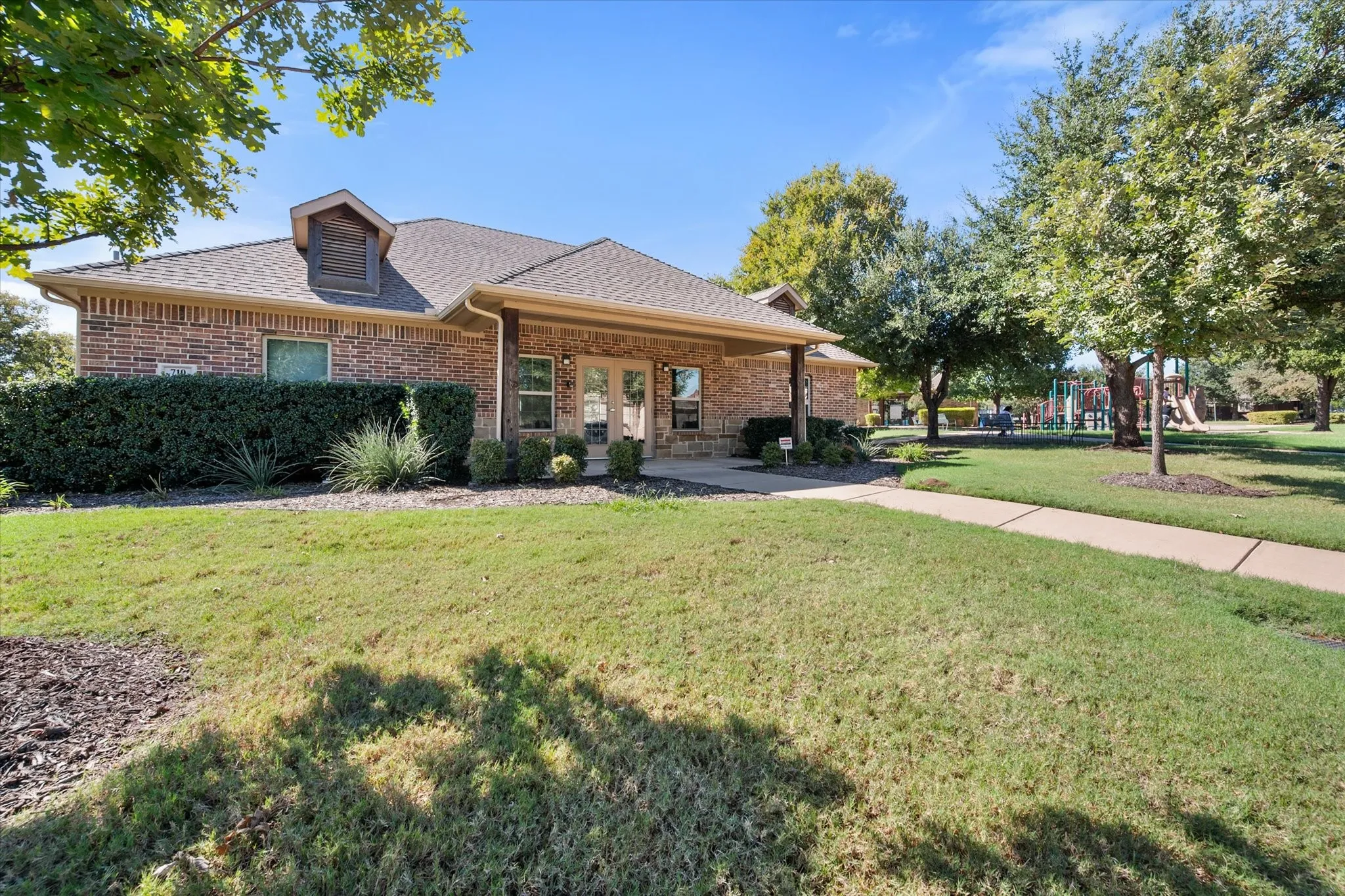 Brick exterior with a dormer, covered entry, front landscaping, and a concrete walkway