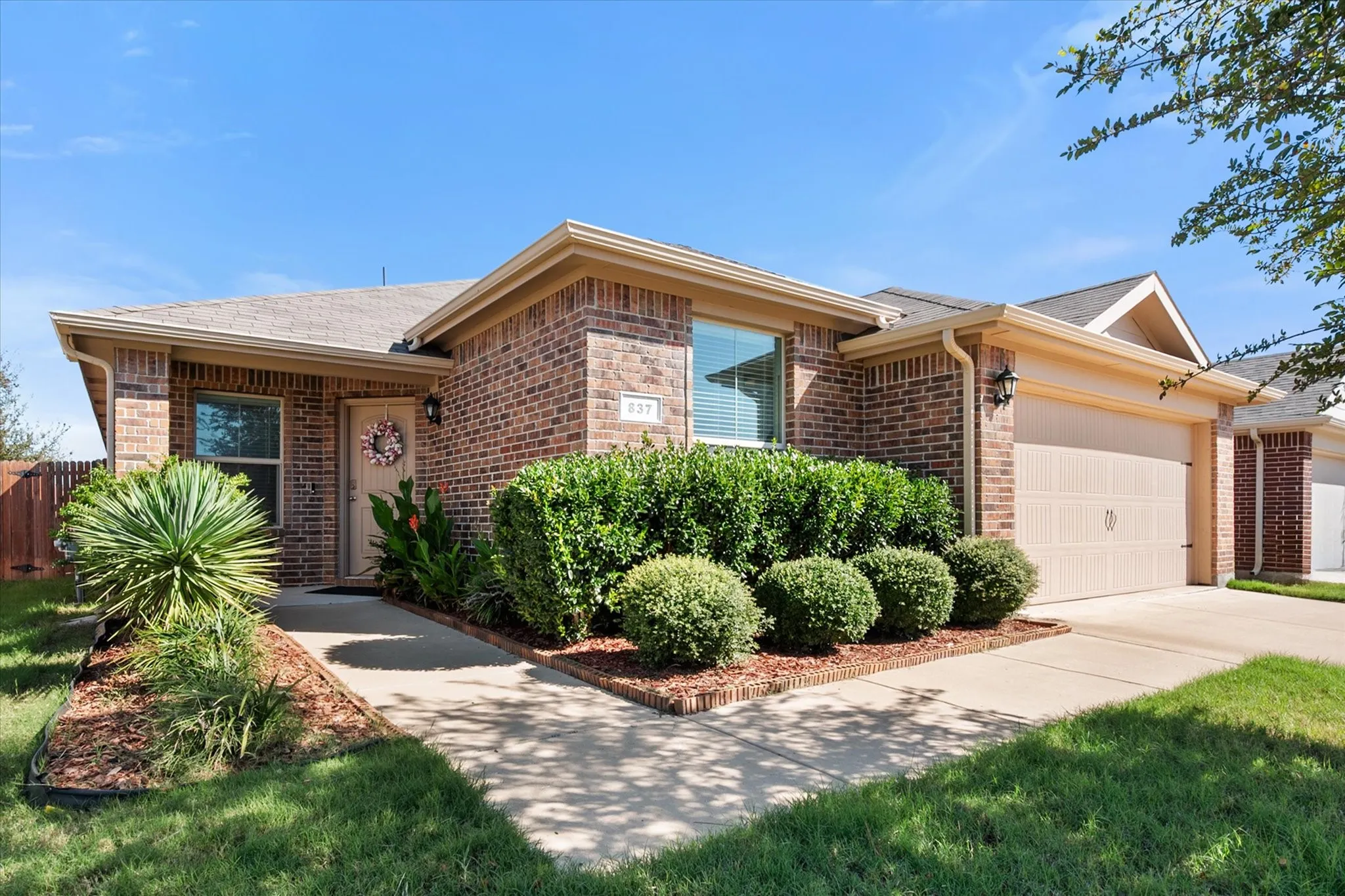 Brick exterior with tan trim, attached garage, well-maintained landscaping, and a concrete walkway