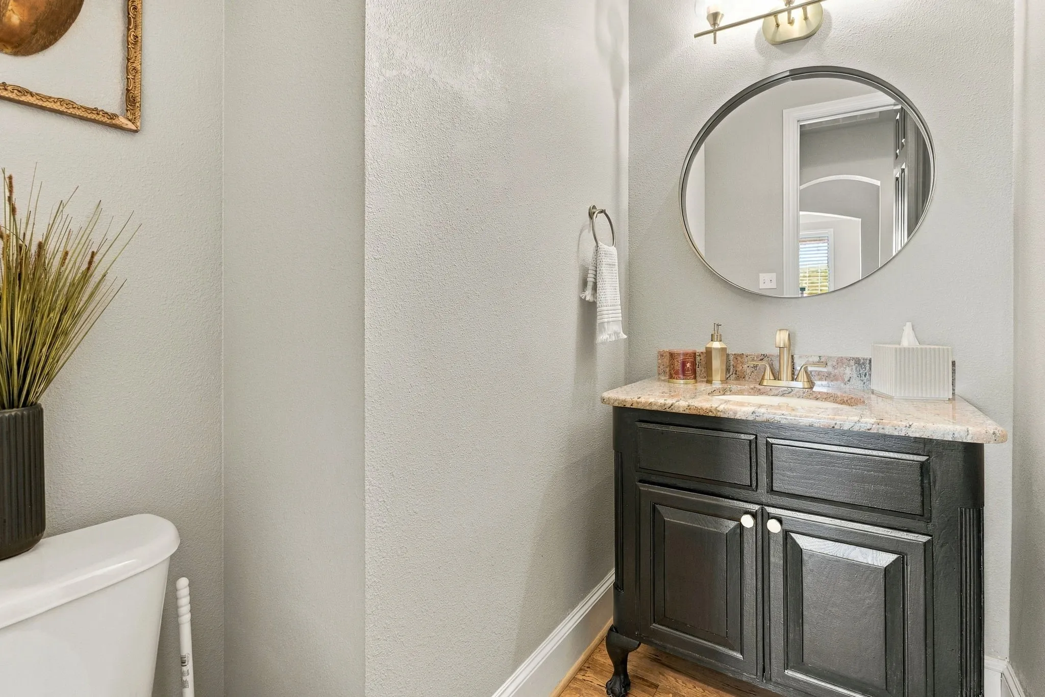 Powder Bathroom | Half bath with a furniture-style vanity, stone countertop and round mirror for main-level convenience.