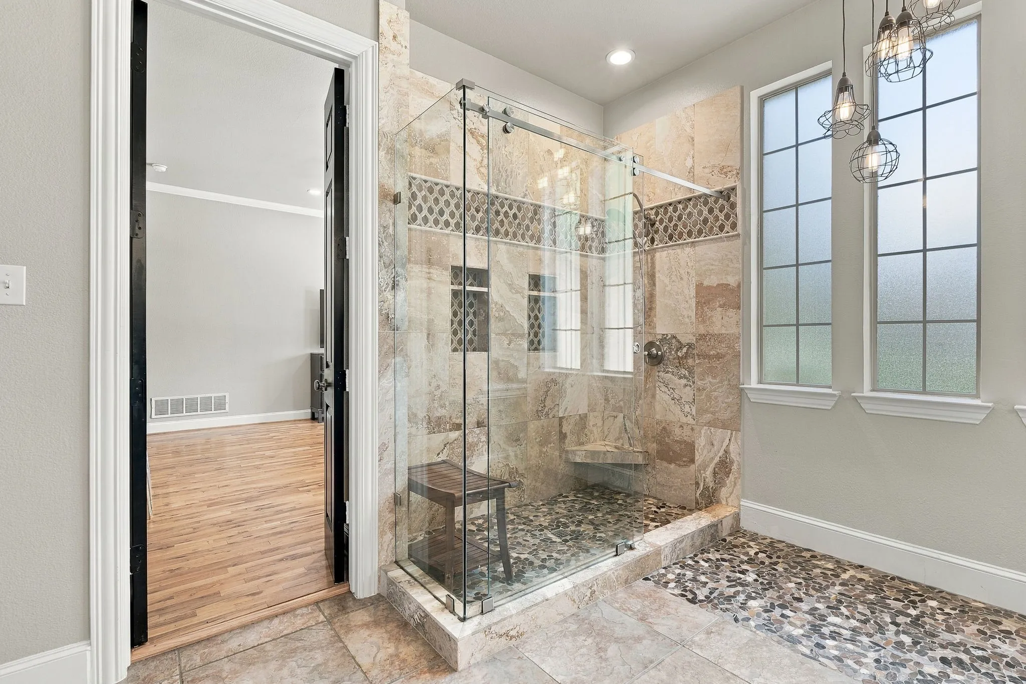 Primary Bathroom Shower | Glass-enclosed walk-in shower with tile surround, built-in bench and nearby windows with shutters.