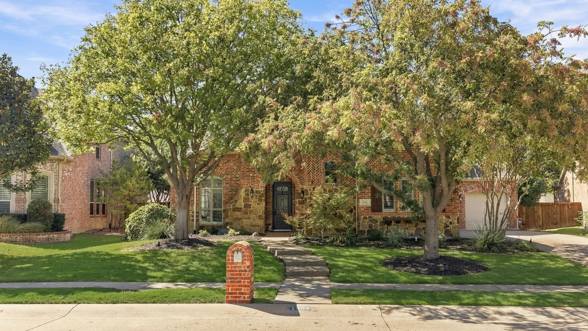 Front Exterior, Daytime | Mature shade trees and landscaped beds frame the front elevation of this Woodhaven II home in Stonebridge Ranch.