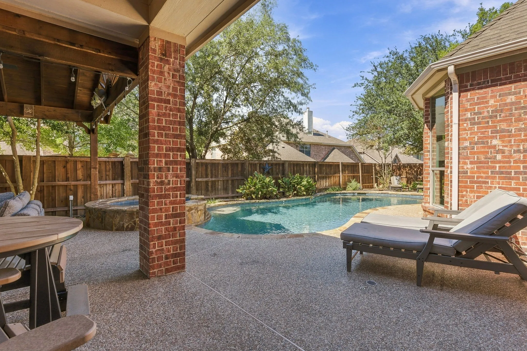 Covered Patio and Pool View | Shaded outdoor living area overlooks the private pool, with brick columns and space for lounging or dining.