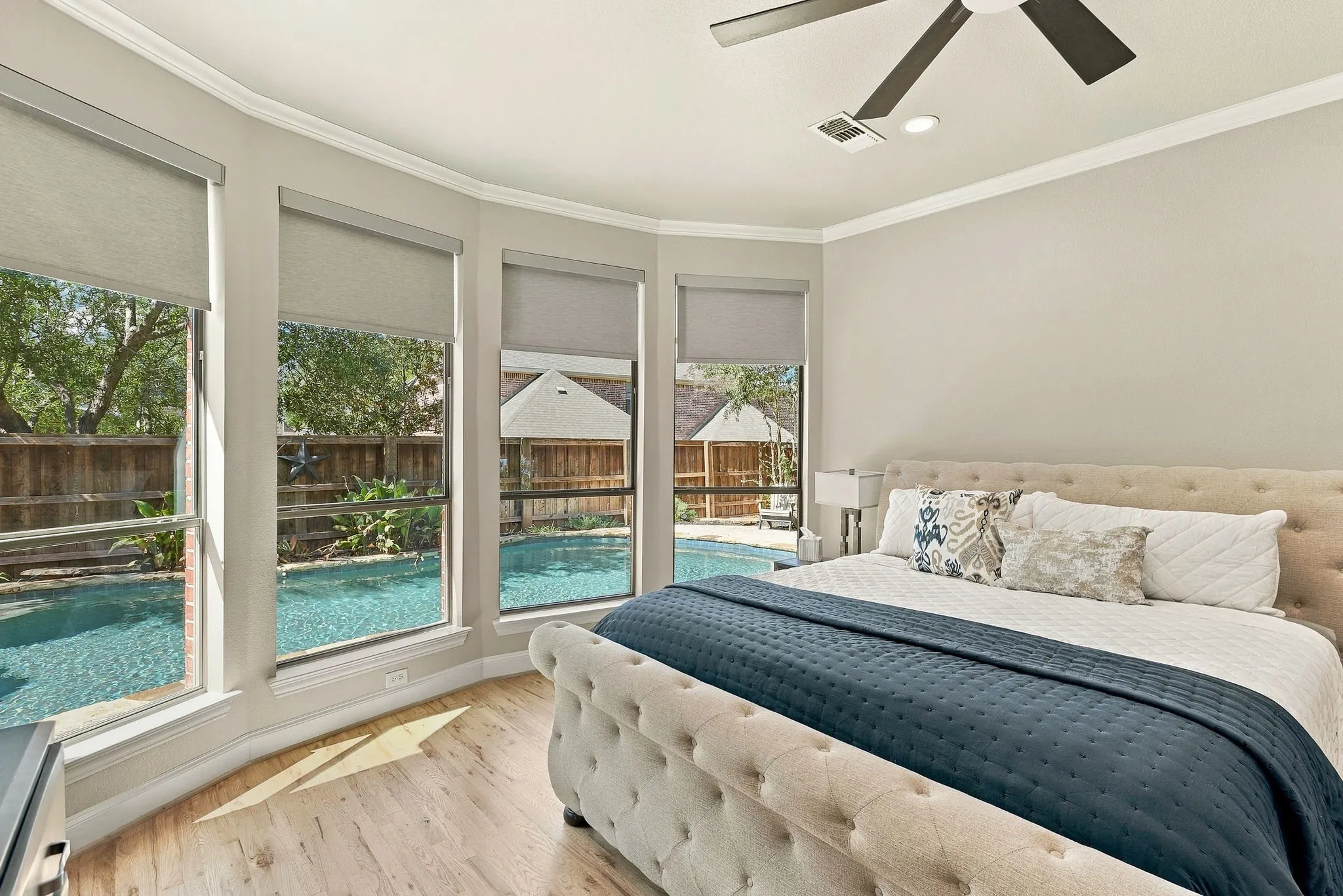 Primary Bedroom, Pool View | A curved wall of windows brings backyard views into the main-level primary suite, featuring wood floors and electric window shades.