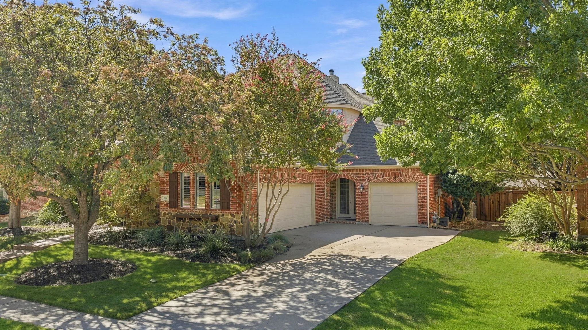 Front Exterior and Garage Approach | Landscaped lawn, mature trees and a broad driveway lead to the three-car garage at 1004 Bristlewood Drive.