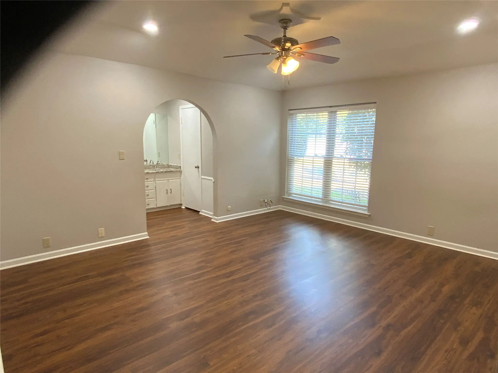 Wood-finish flooring, recessed lighting, ceiling fan with integrated light, and an arched doorway