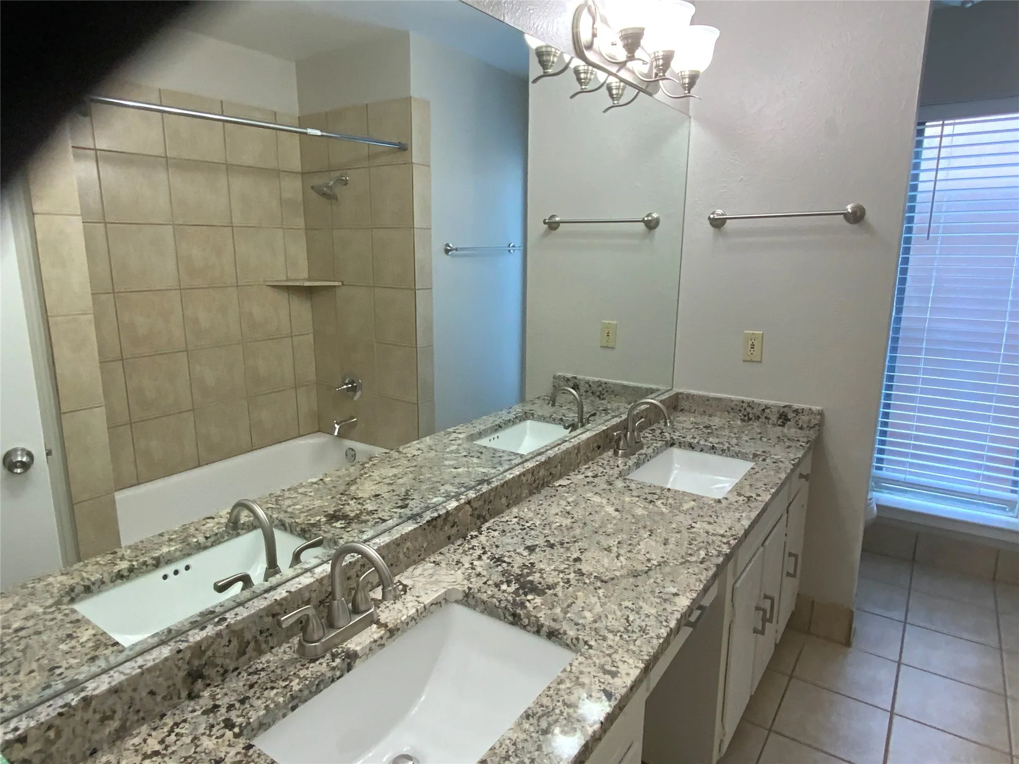 Dual vanity with granite-style countertop and undermount sinks, full-width mirror, tile flooring, and a shower-tub combination with tile surround