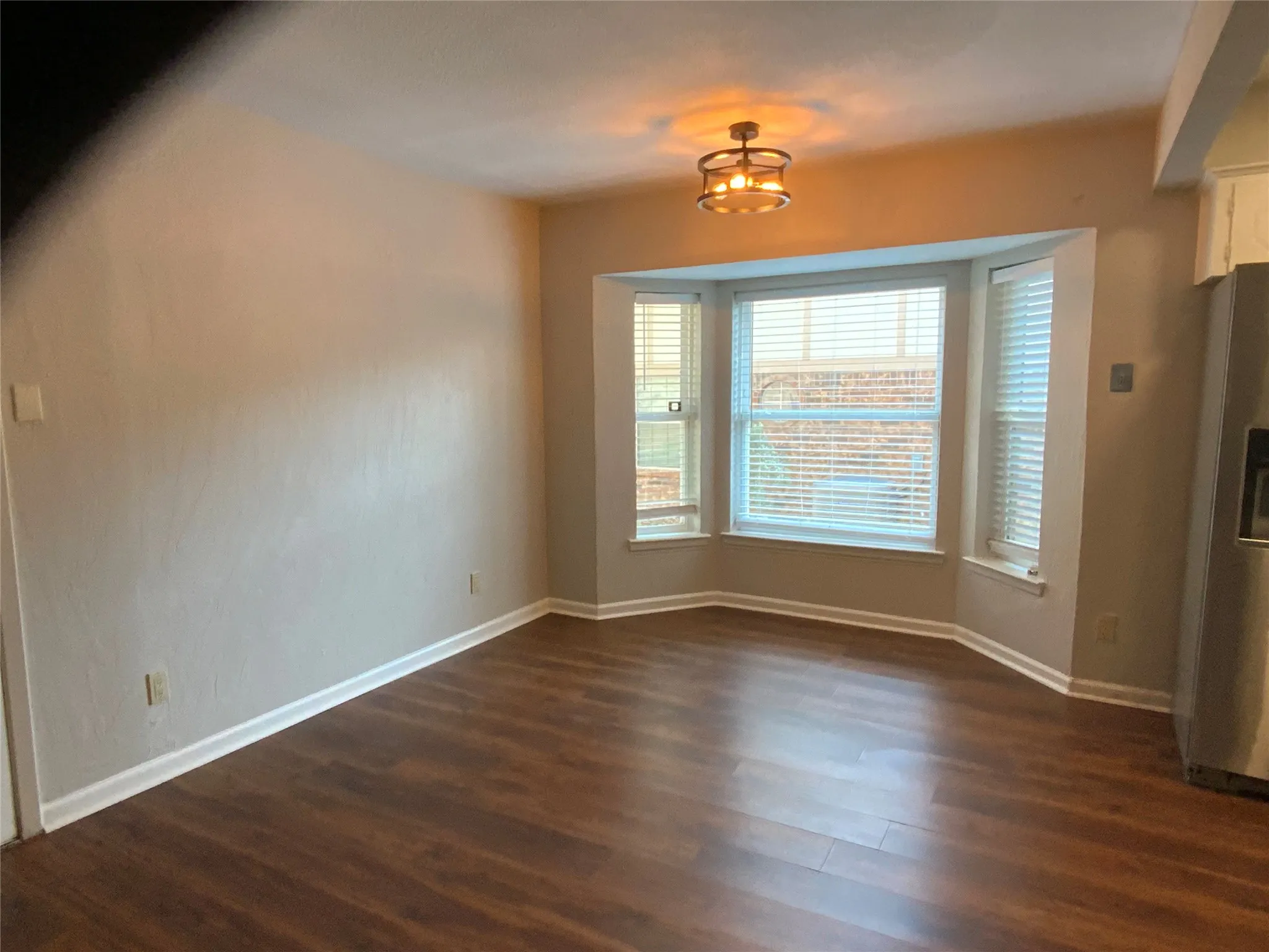 Bay window with horizontal blinds, wood-finish flooring, and a semi-flush mount ceiling fixture