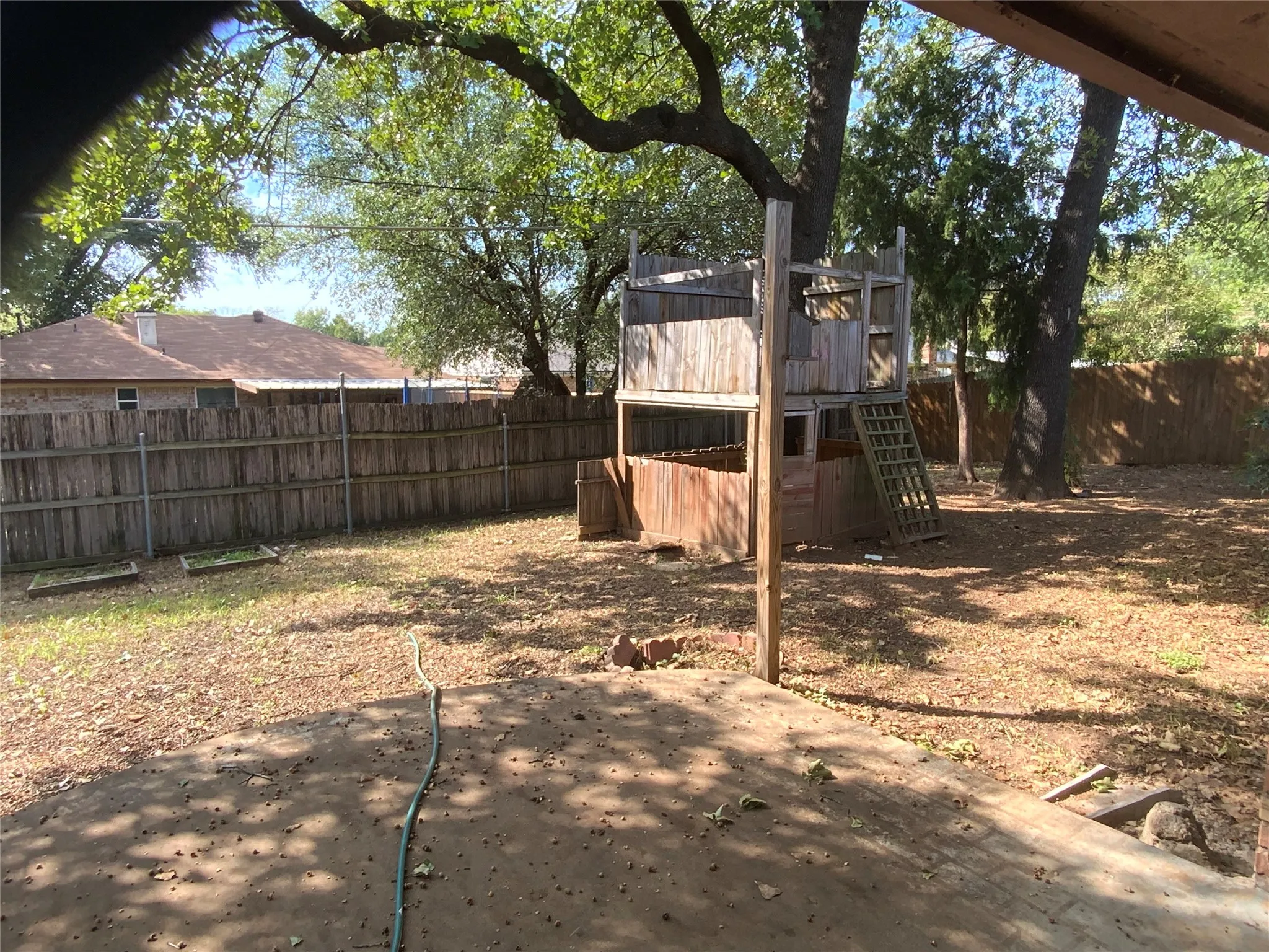 Expansive backyard featuring a wood privacy fence, mature trees, and a multi-level wood play structure