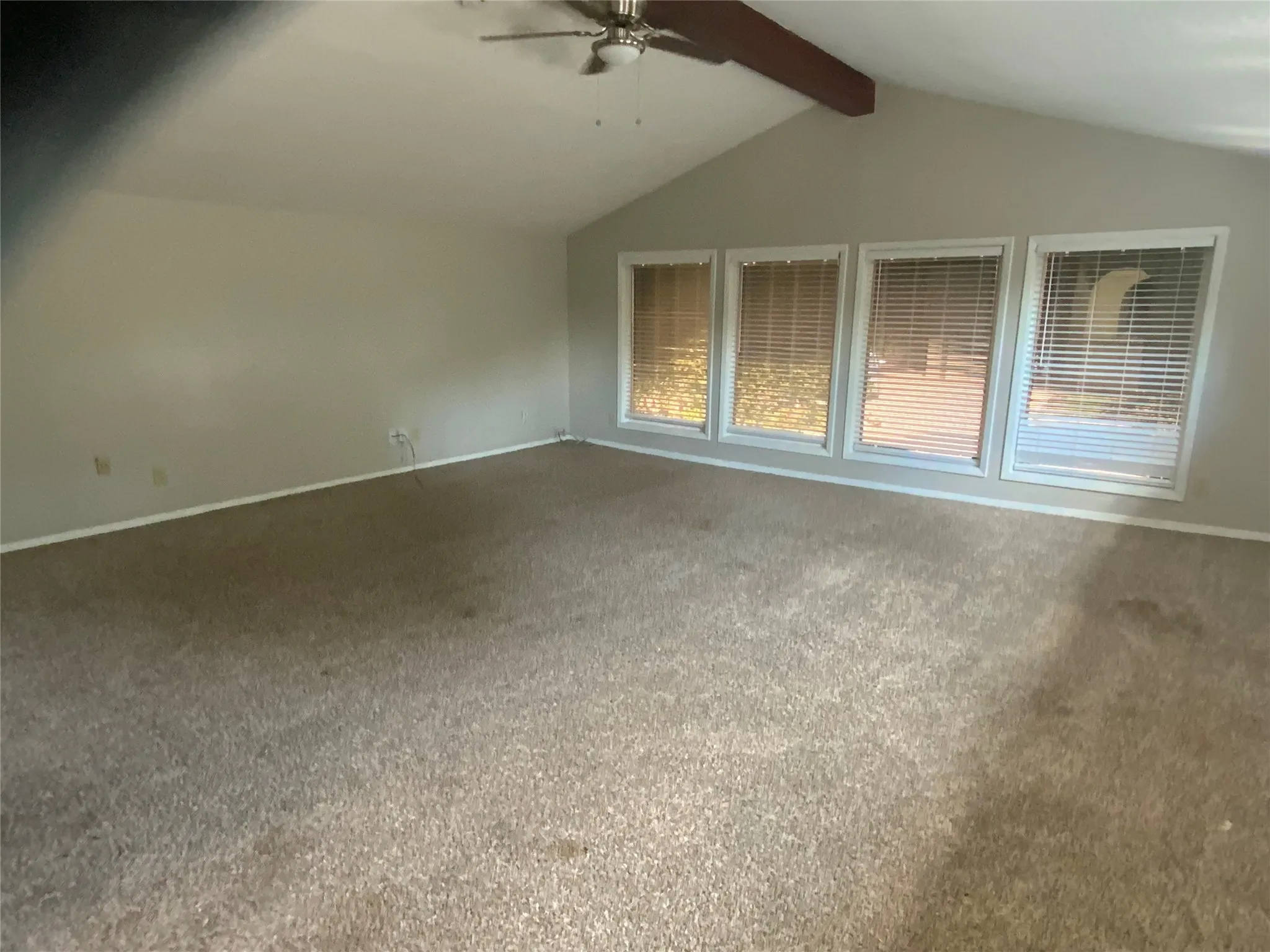 Vaulted ceilings with an exposed beam, multiple windows with blinds, and a ceiling fan