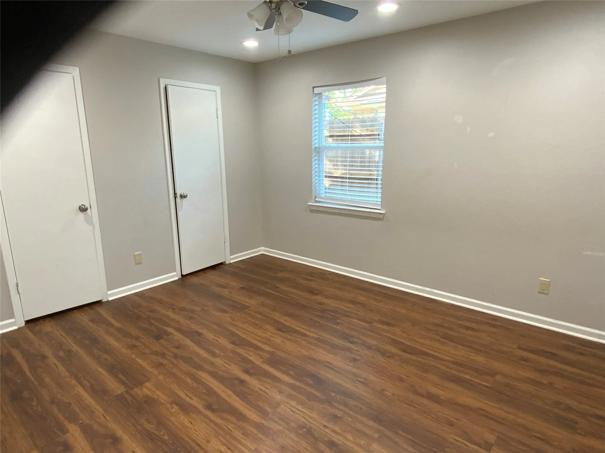 Wood-finish flooring, recessed lighting, ceiling fan, window with blinds, and two solid panel doors
