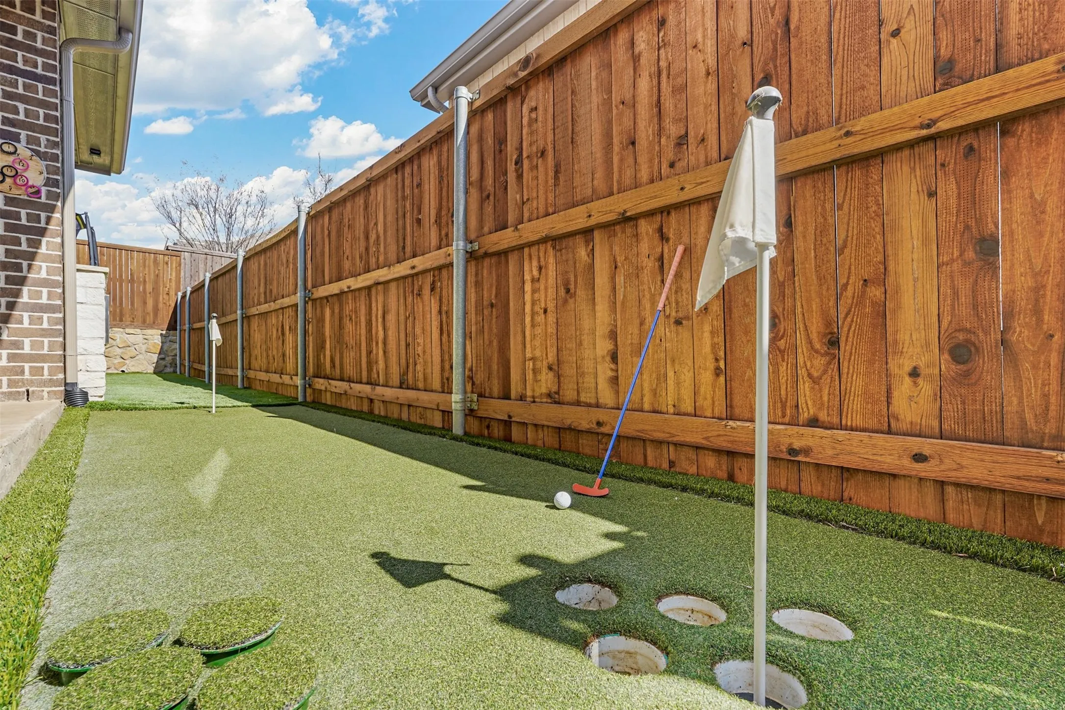 Putting green with artificial turf, wood fence, and brick exterior