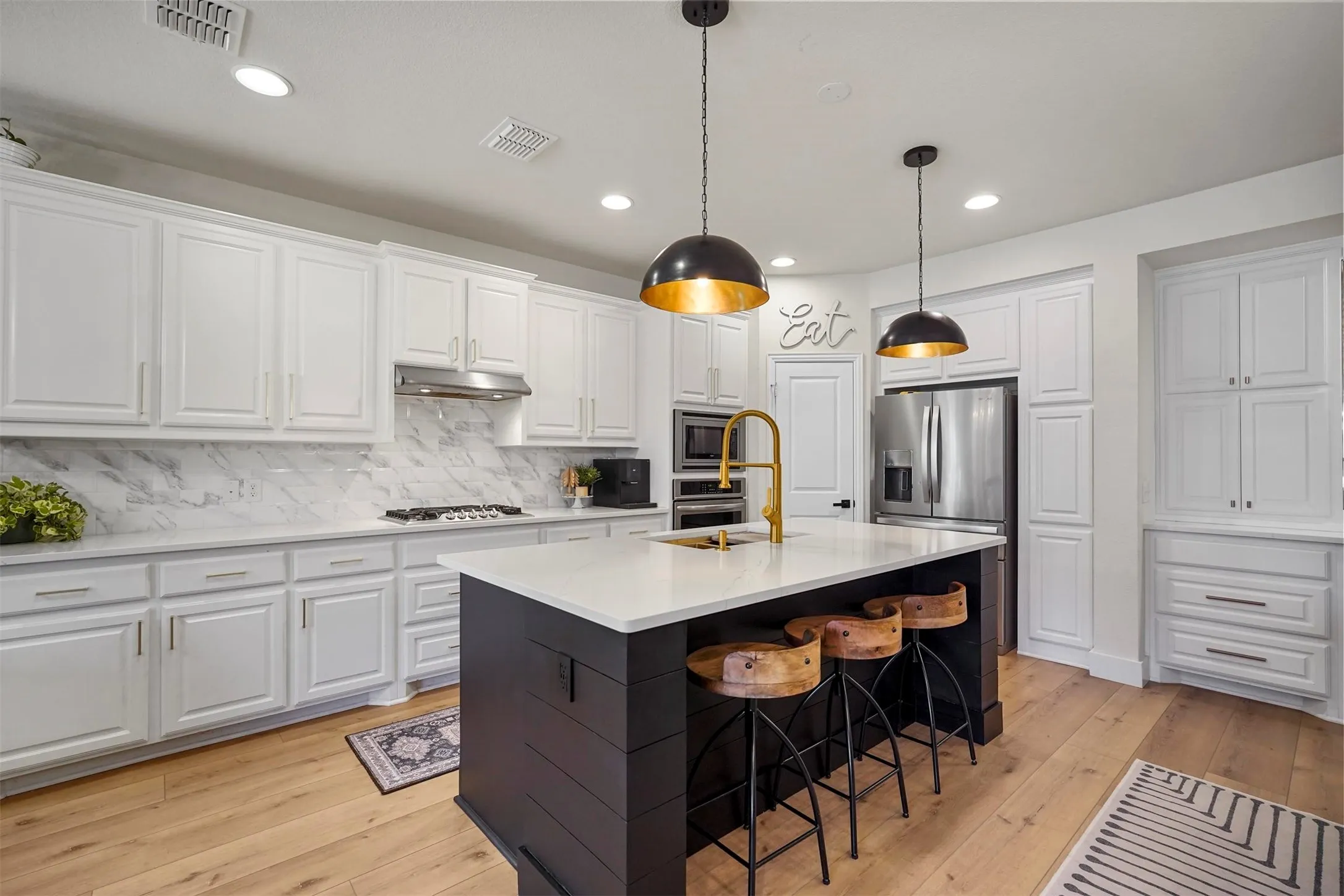 Gourmet kitchen with a large center island, white shaker-style cabinetry, stainless steel appliances, and wood-finish flooring