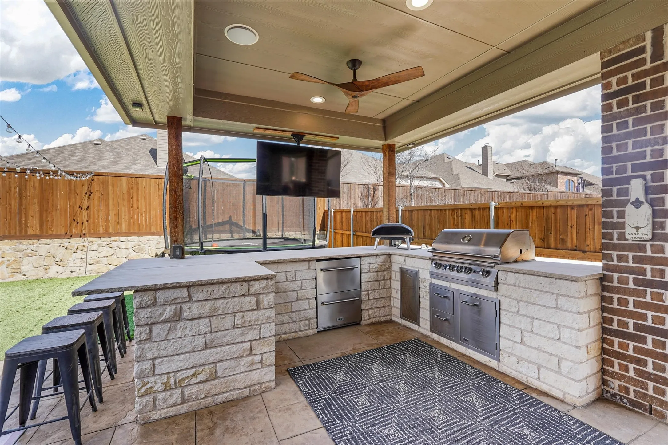 Covered patio featuring an outdoor kitchen with built-in grill, stone veneer construction, and integrated ceiling fan