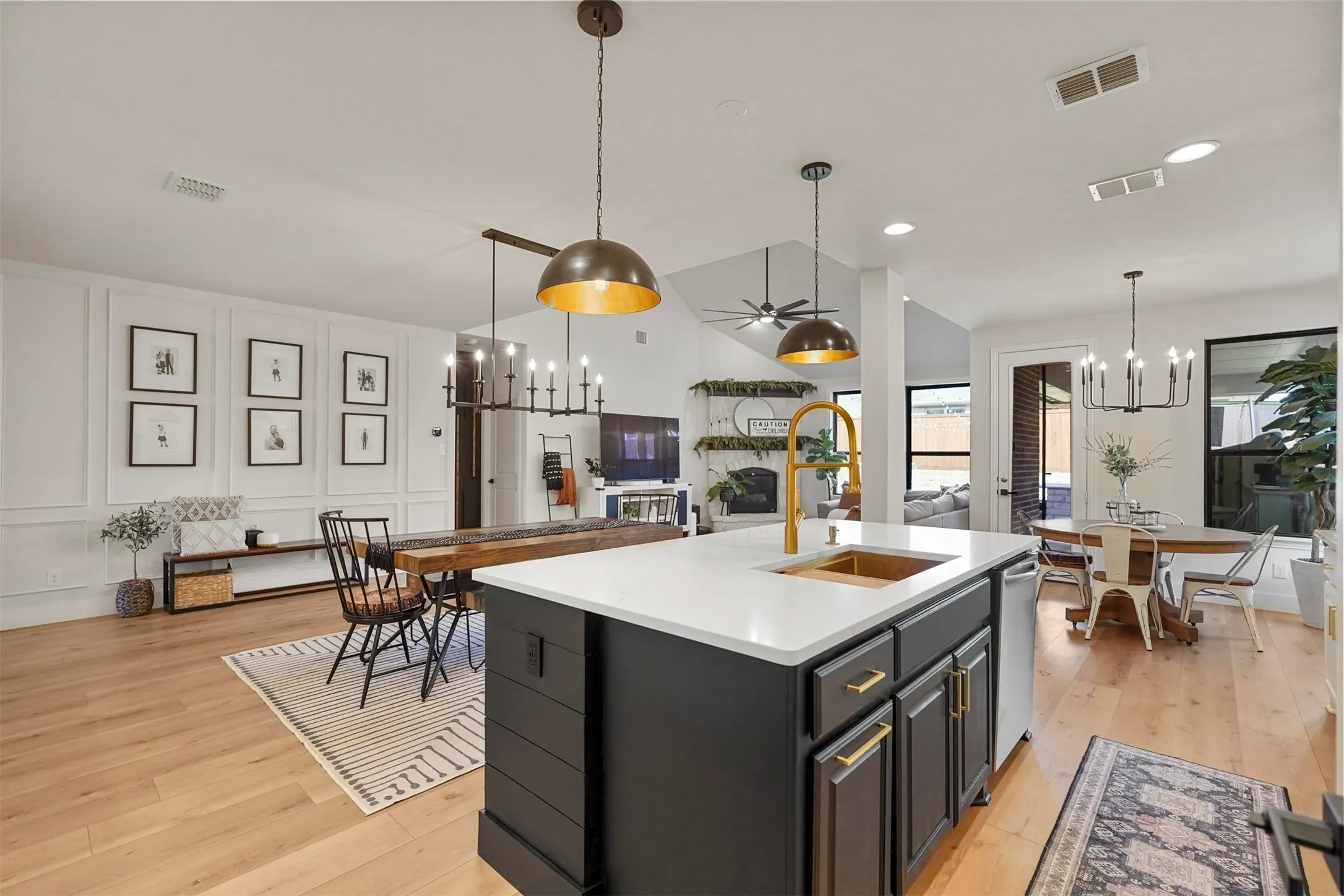 Kitchen island with a white countertop and gold-finish fixtures, wood-finish flooring, a vaulted ceiling, a chandelier, and panel molding