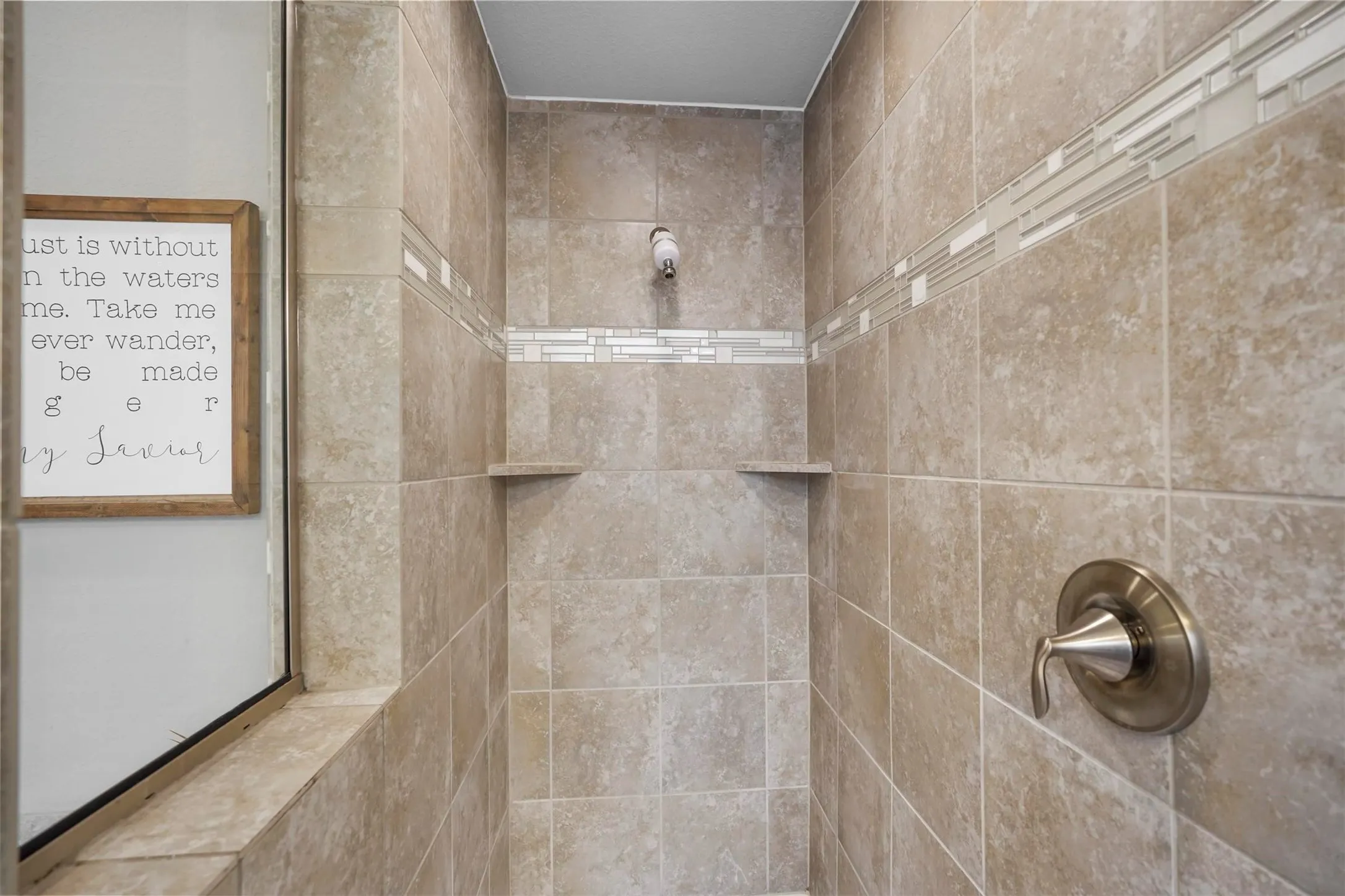 Tiled shower with decorative accent banding, built-in shelving, and a brushed nickel shower fixture