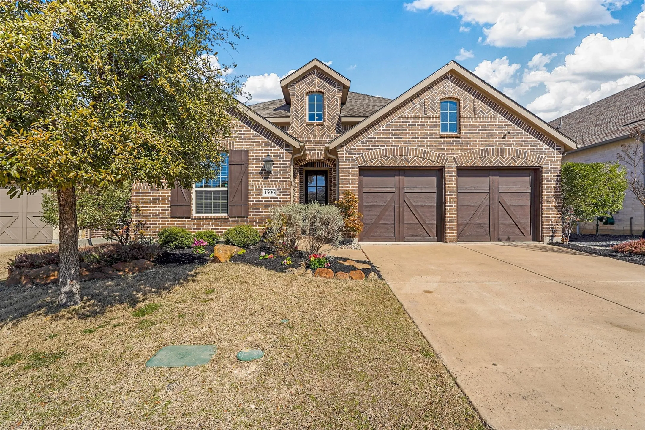 Brick facade with decorative arched lintels, two-car garage with wood-finish doors, landscaped front yard, and a concrete driveway