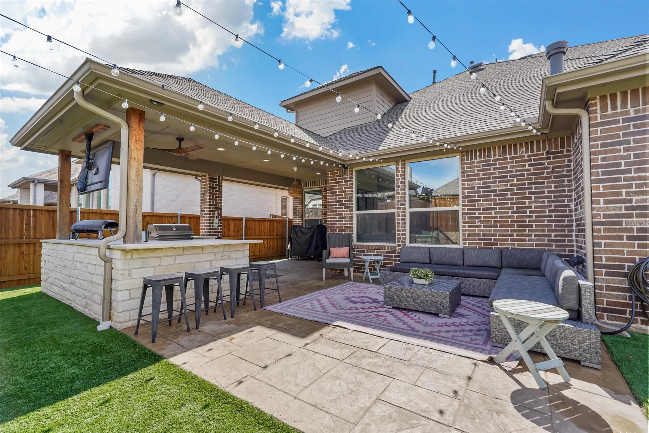 Expansive patio featuring a built-in outdoor kitchen with stone-finish base, covered seating area, and stamped concrete flooring