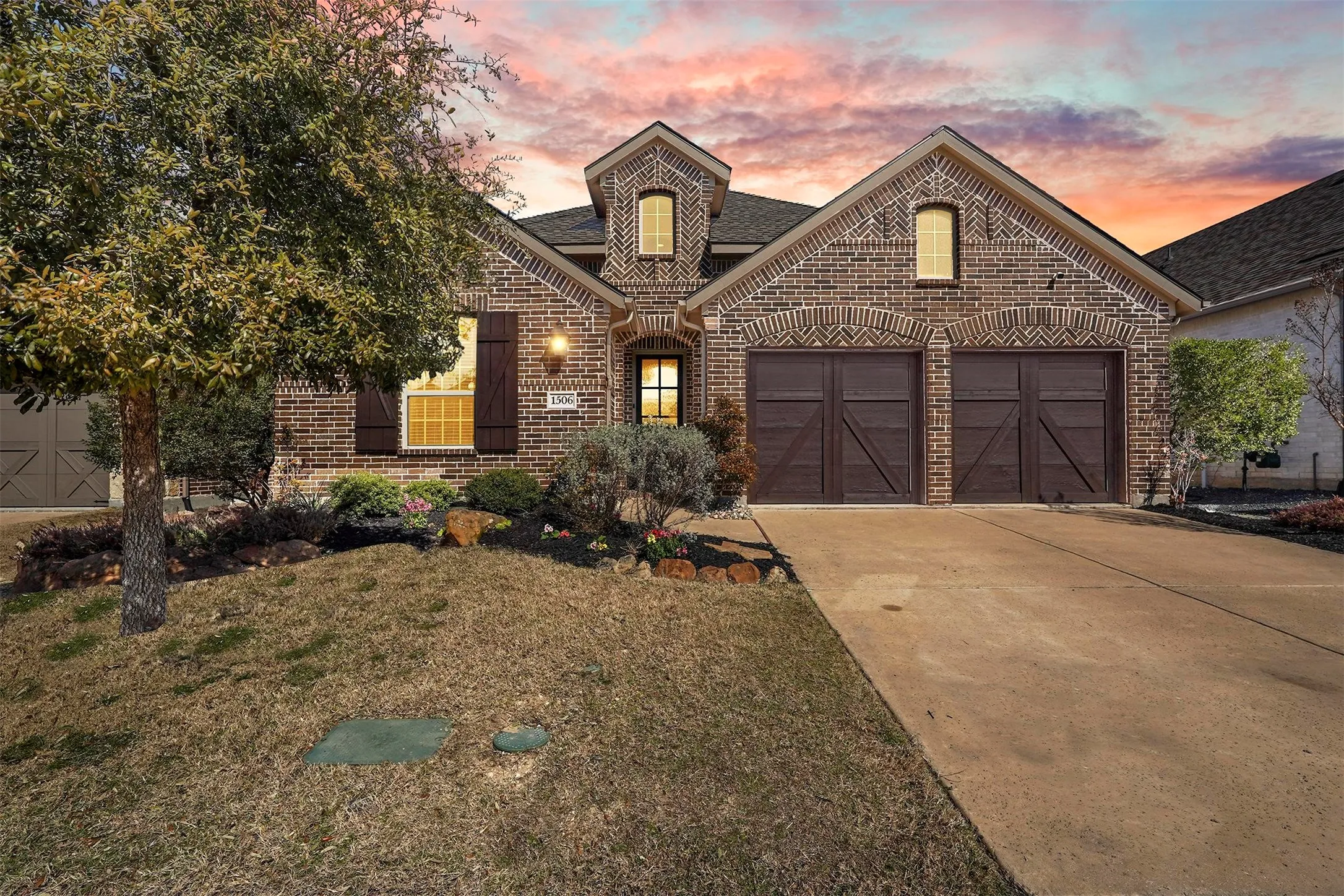 Brick exterior with architectural details, two-car garage with wood-finish doors, landscaped front yard, and a concrete driveway