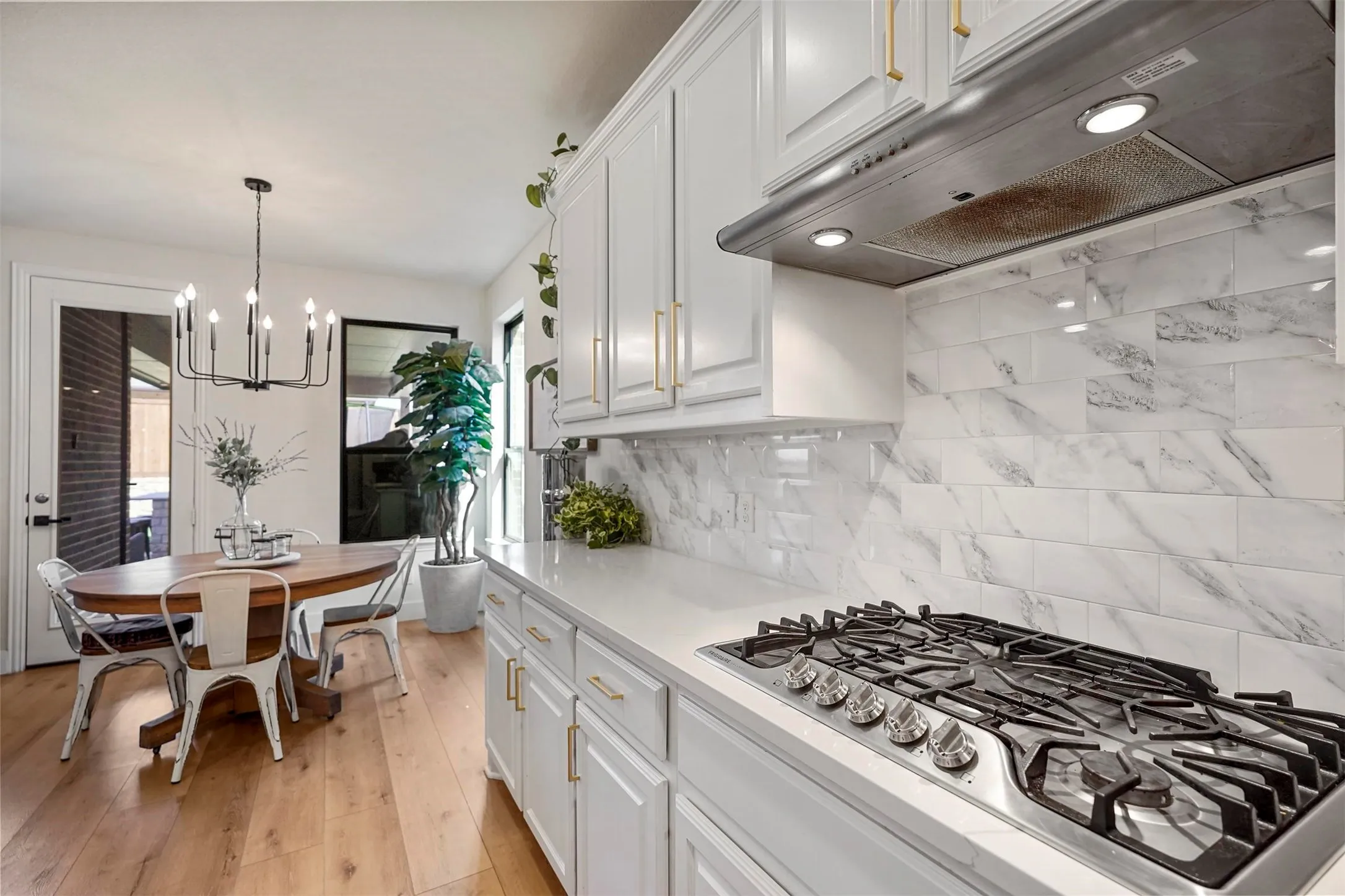 White upper and lower cabinetry with gold-finish hardware, stainless steel gas cooktop, quartz countertop, and white subway tile backsplash