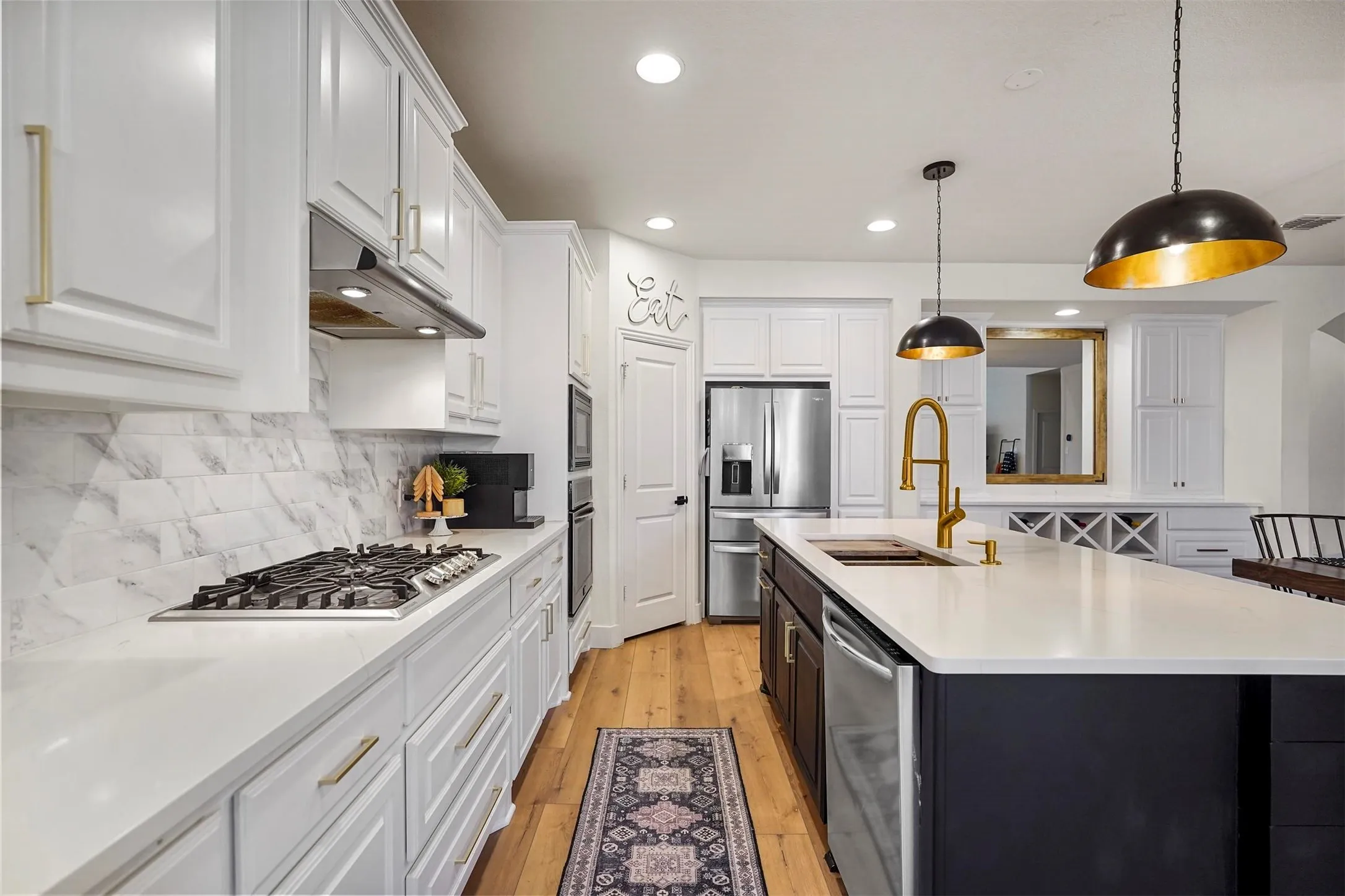 White cabinetry with gold-tone hardware, wood-finish flooring, white countertop surfaces, and a built-in stainless steel gas range