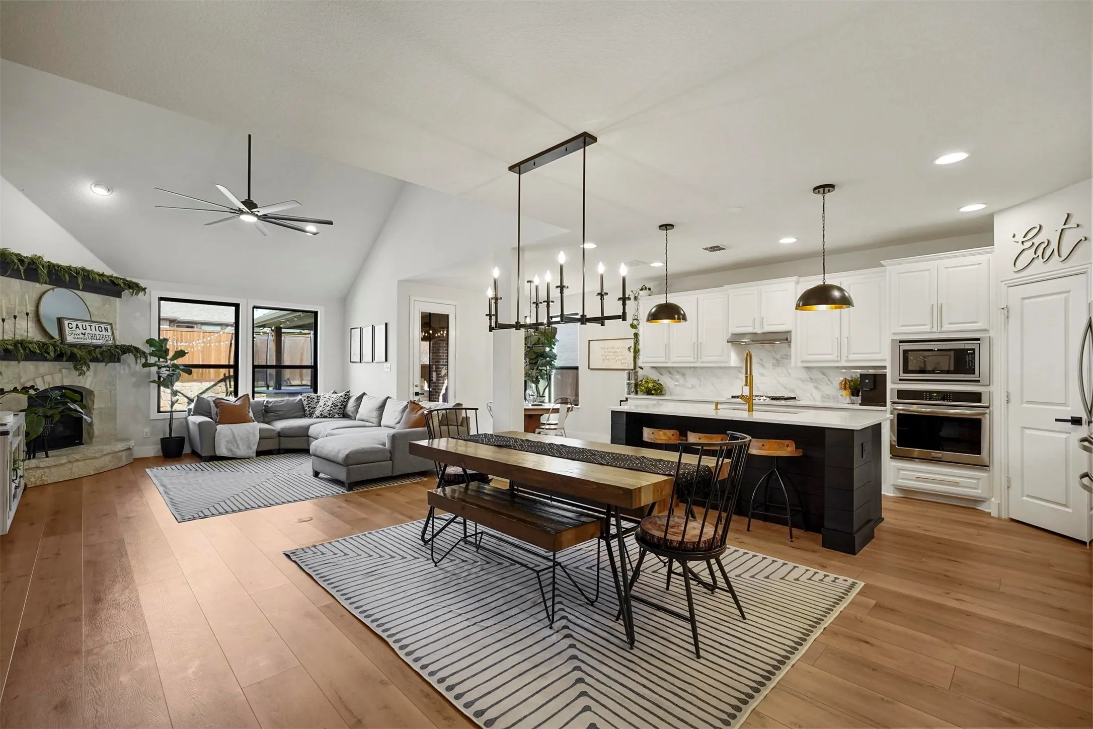Open-concept living space featuring wood-finish flooring, a vaulted ceiling, and a stone-clad fireplace