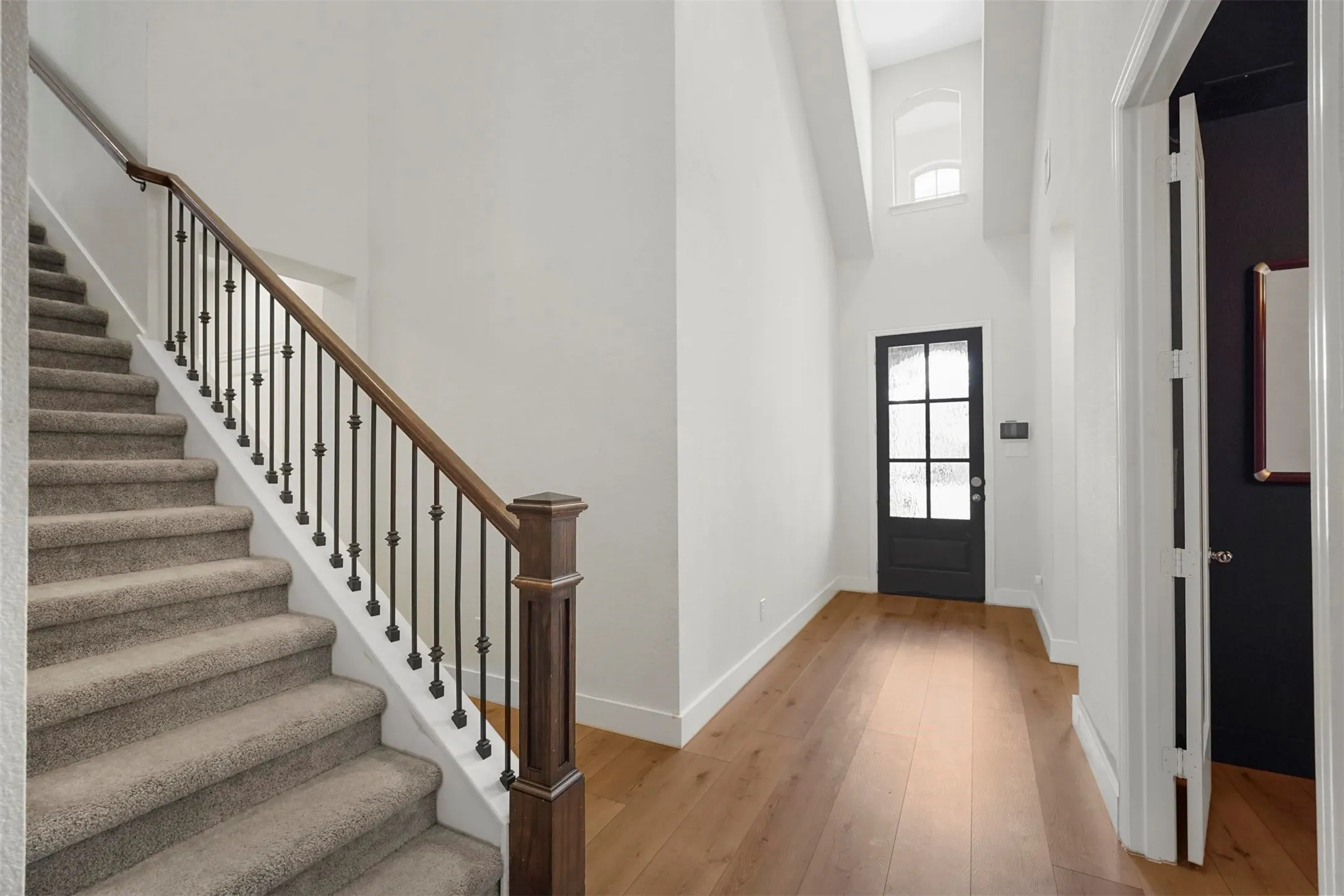 Two-story foyer with high ceilings, wood-finish flooring, and a black paneled door with frosted glass
