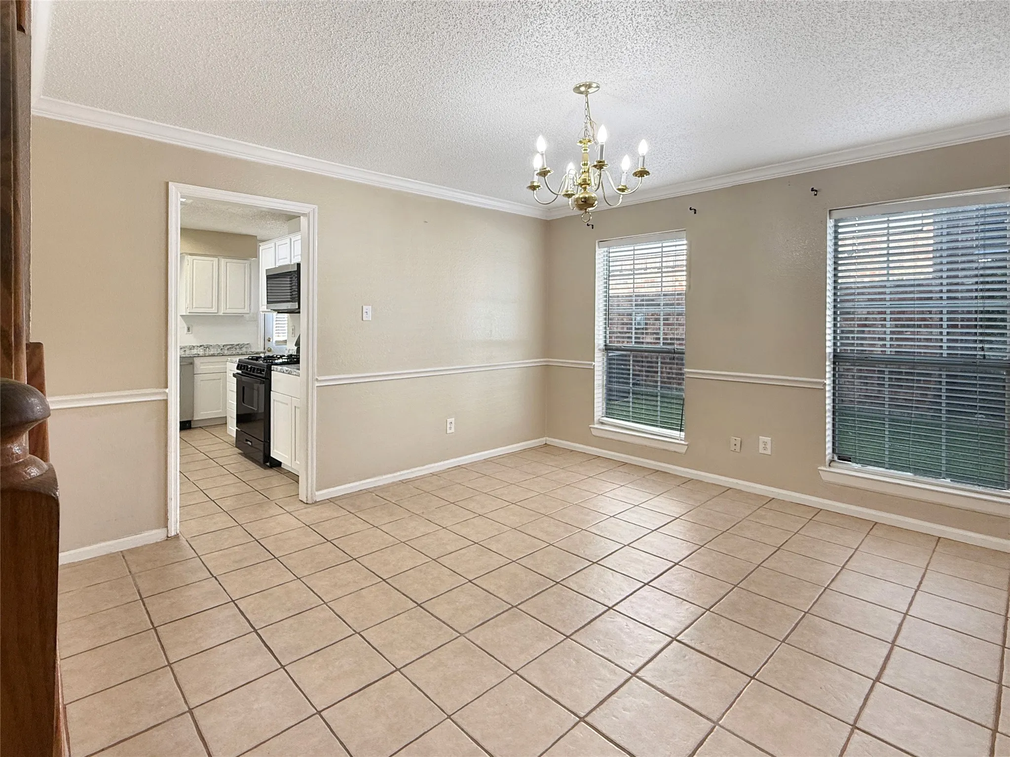 Tile flooring, crown molding, chair rail molding, two windows with blinds, and a chandelier