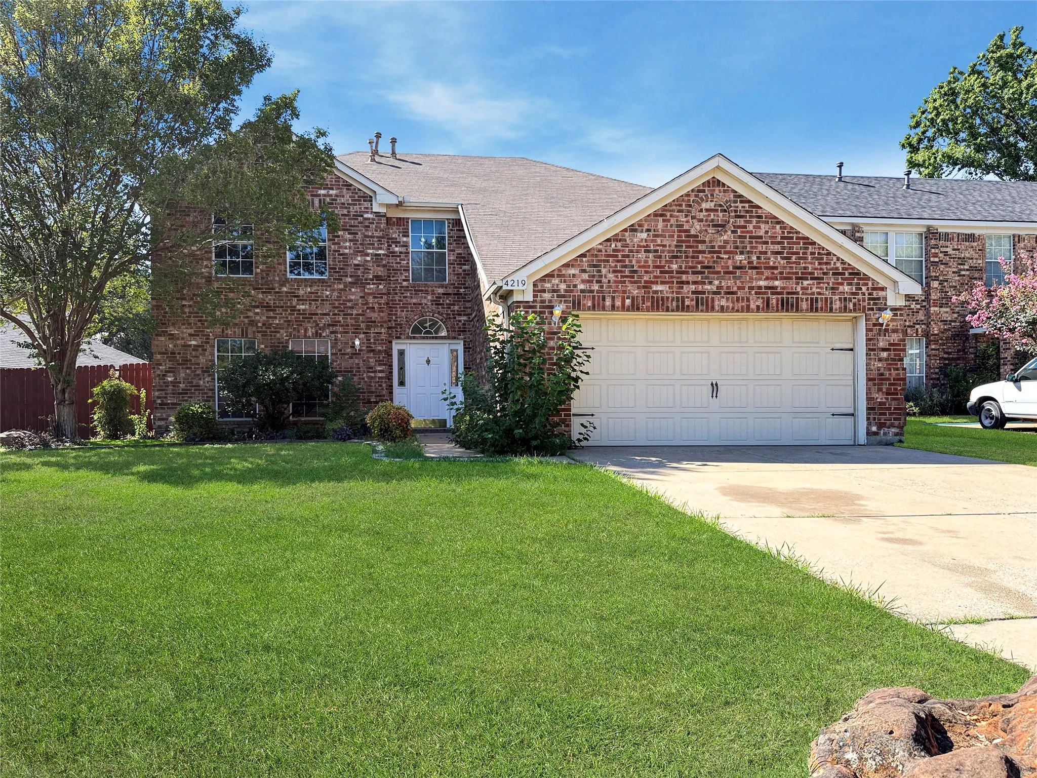 Brick exterior featuring a gabled roofline, an attached two-car garage, and a white front door with an arched transom window