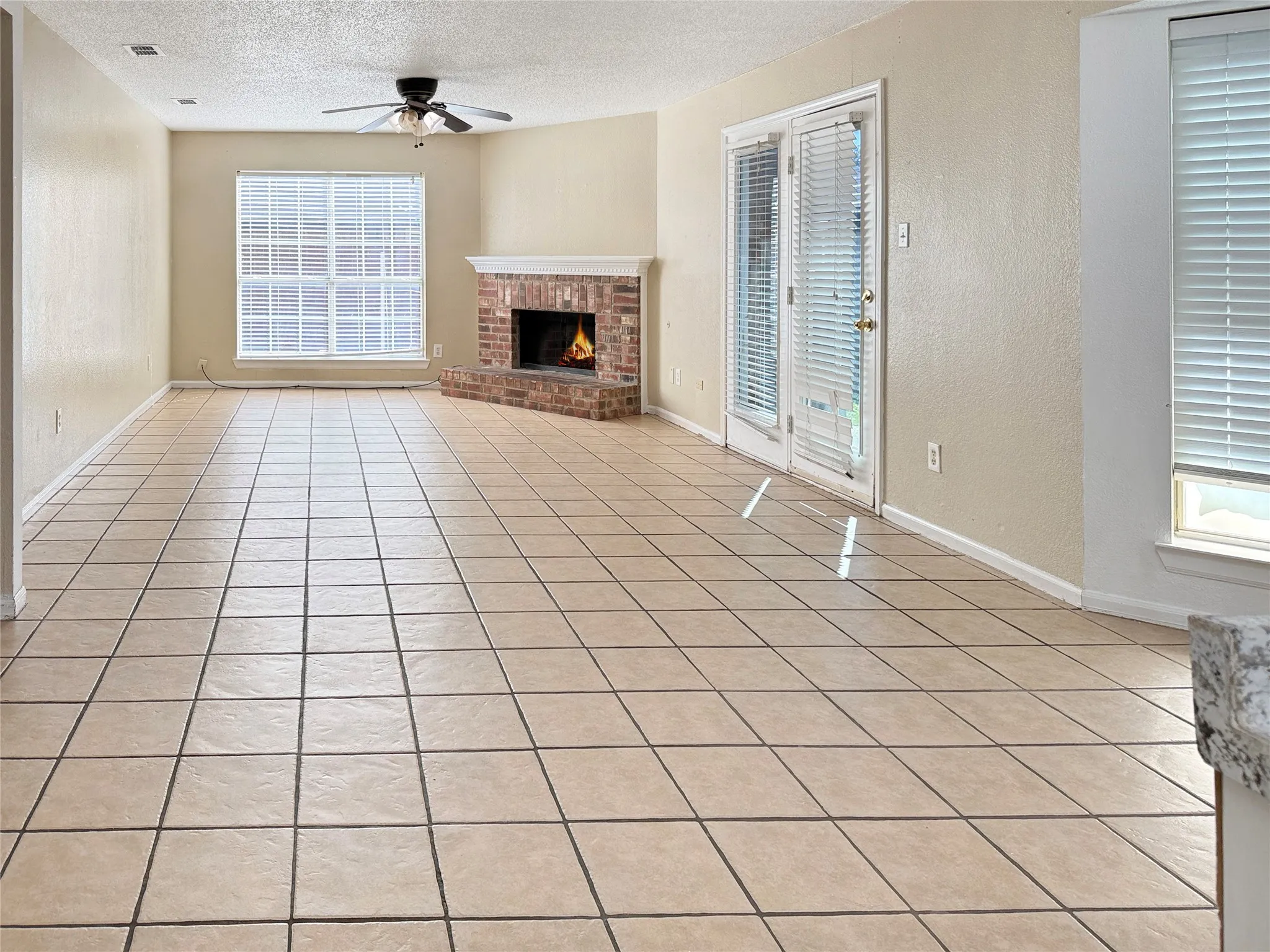 Expansive tiled flooring, corner brick fireplace with mantel, ceiling fan, and French doors