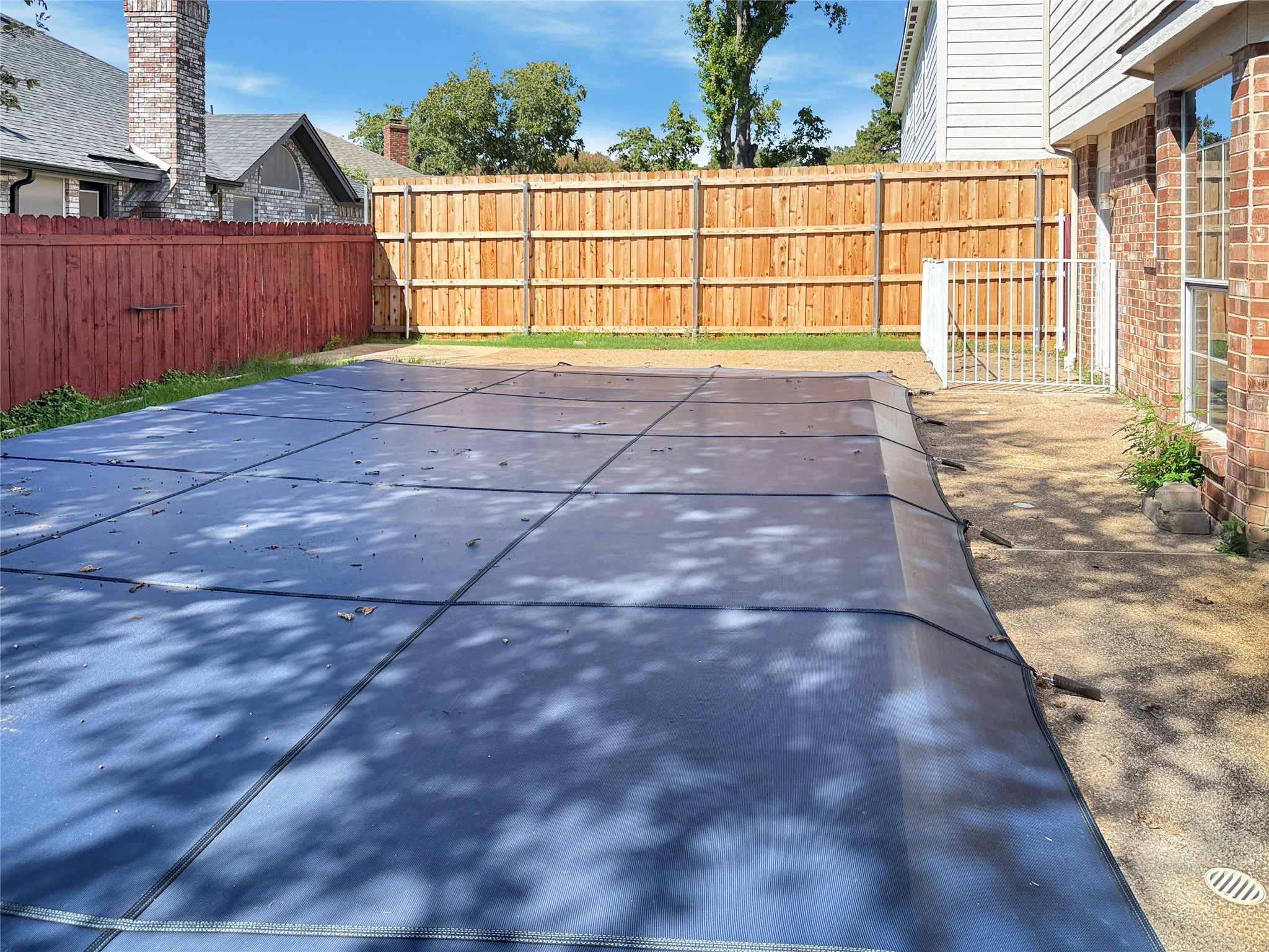 Private backyard with a pool cover, brick exterior, and wood fencing