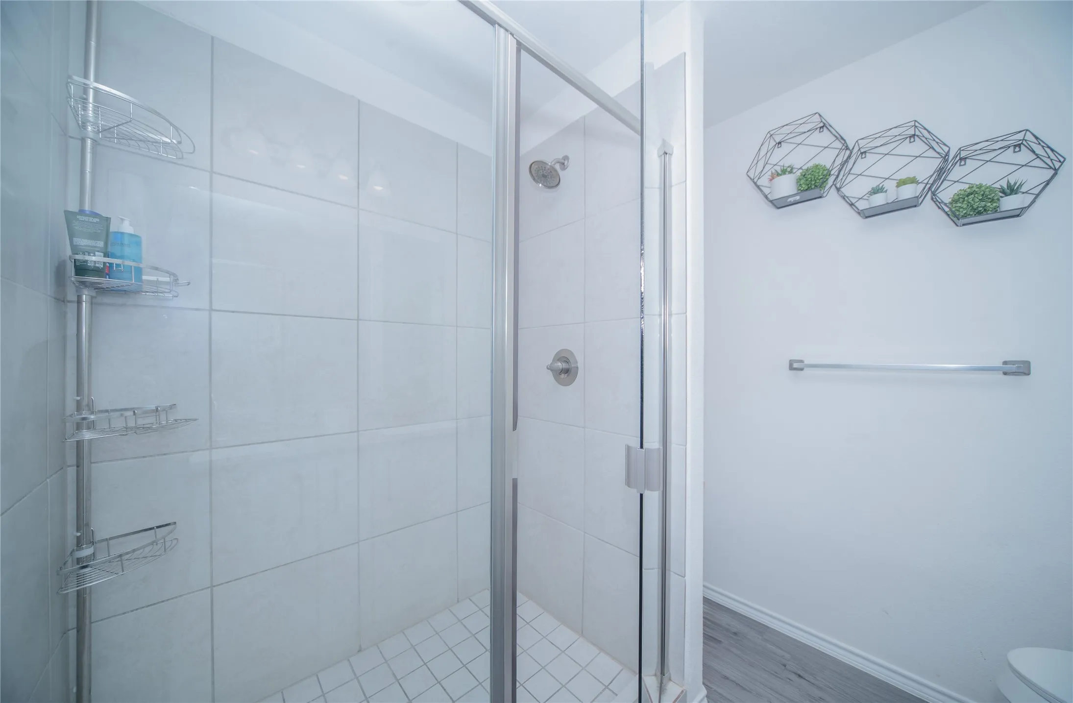 Shower with glass enclosure, white tiled walls, and a tiled floor