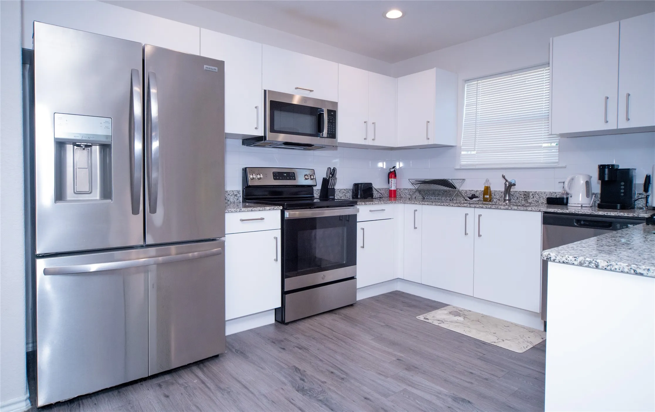 Stainless steel appliances, white cabinetry, light-toned wood-finish flooring, white subway tile backsplash, and speckled countertops